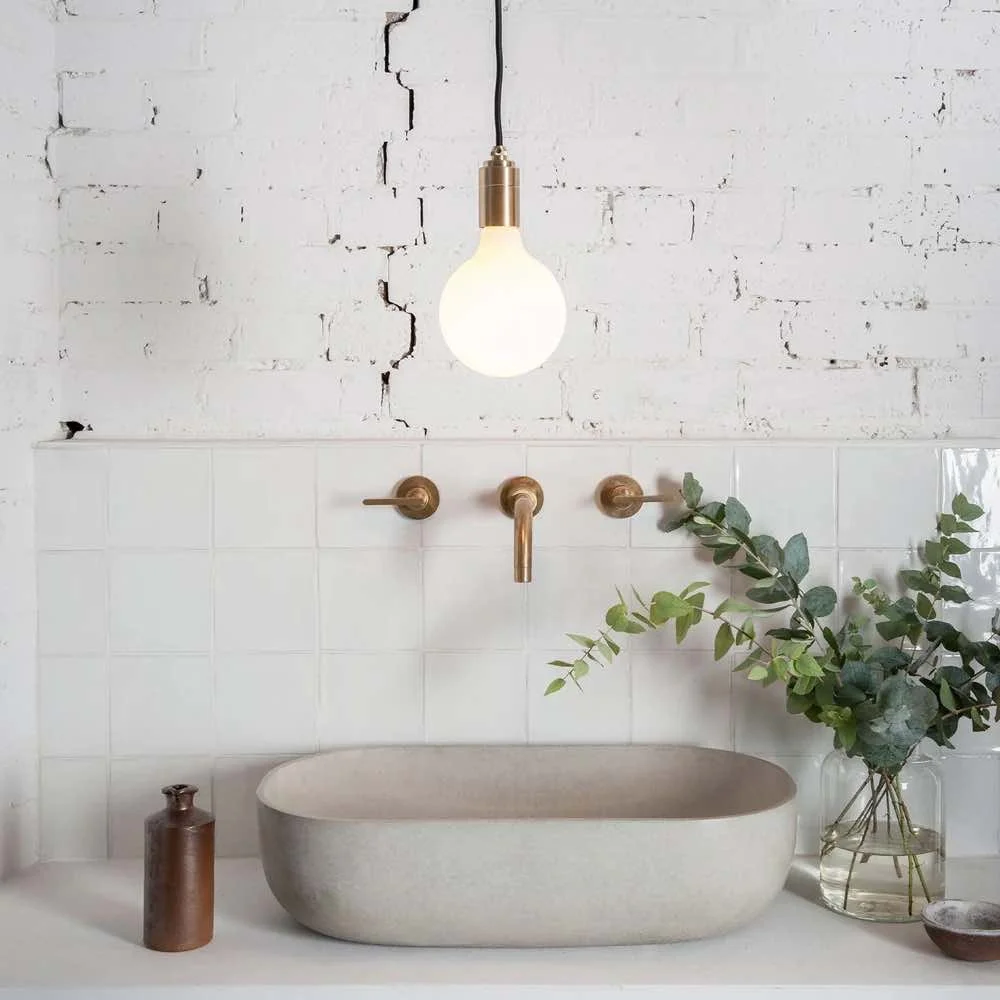 sphere lightbulb hanging over a grey concrete basin with white tiles and white brick wall behind it.