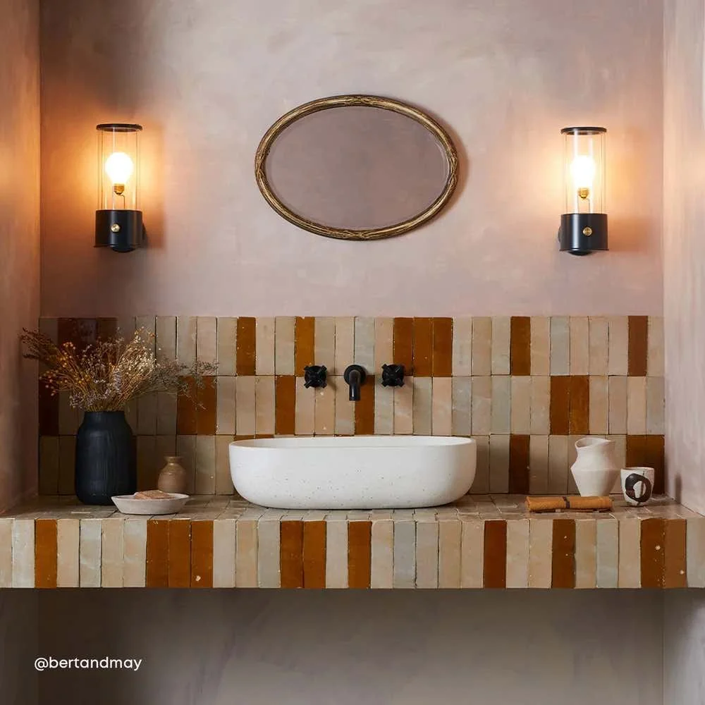bathroom basin on beige and burnt orange tiled vanity unit. with two lantern style lights either side of mirror above basin.