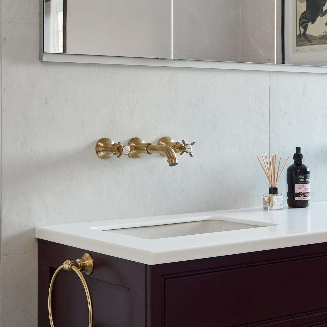 Gold wall mounted tap above white basin in grape coloured vanity unit