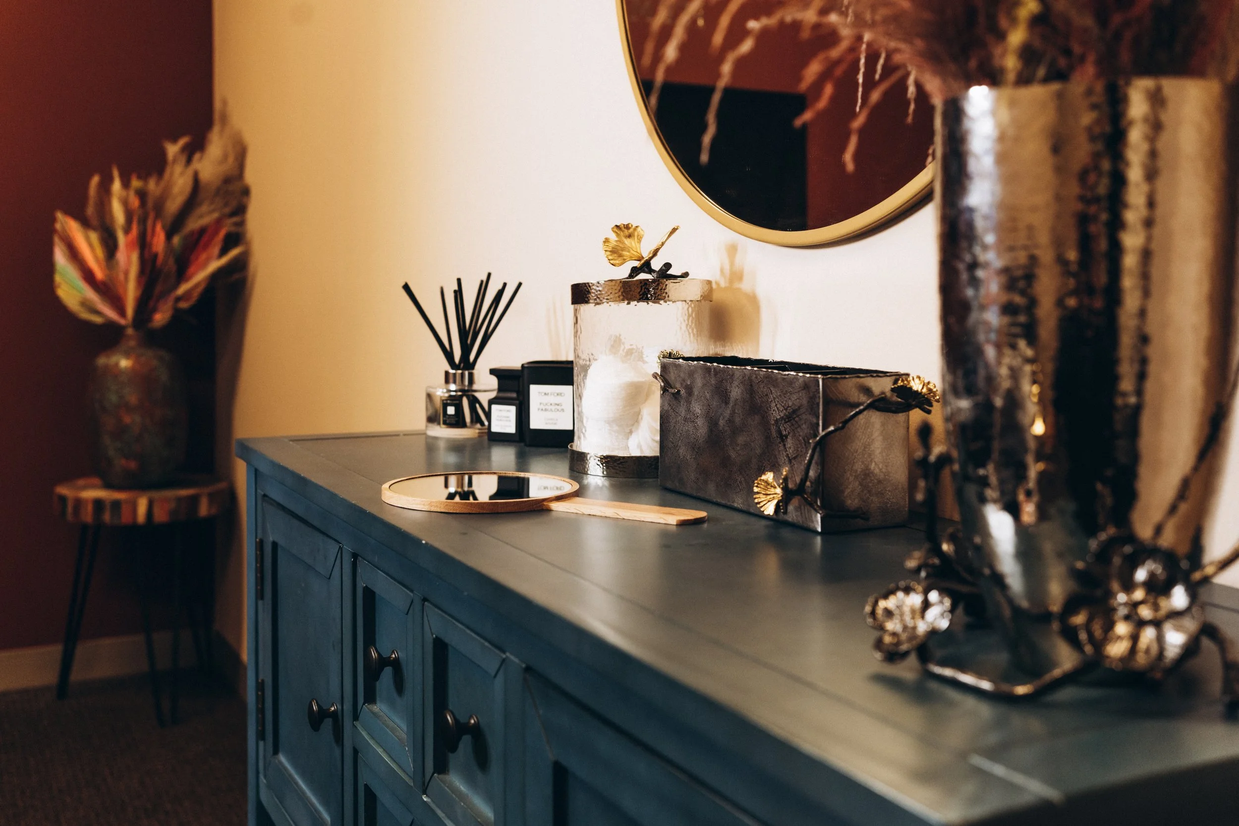 Decorative items on a dark blue sideboard, including a mirror, vases, a perfume set, and a tray in a cozy room.