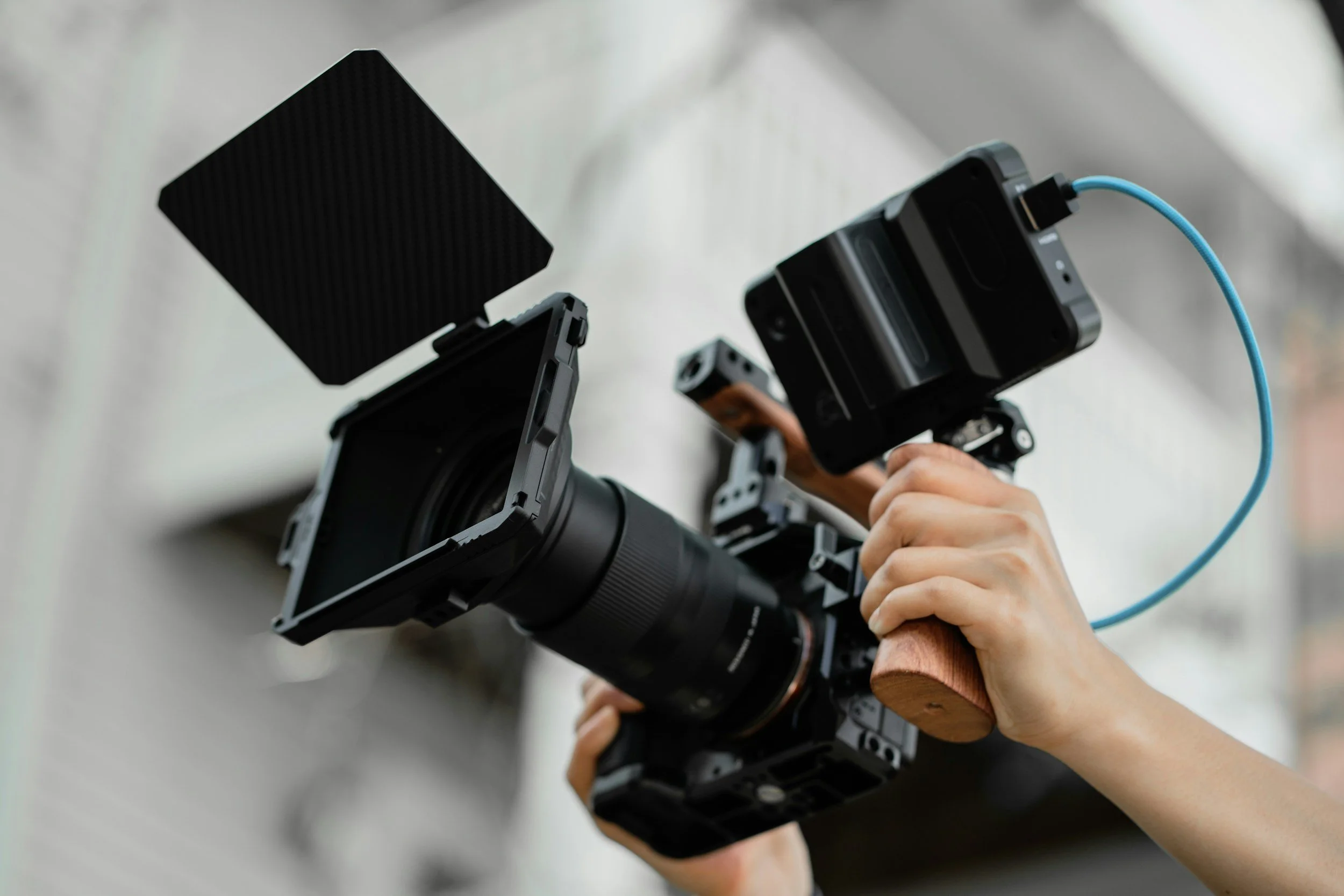 Person holding a professional camera with an external microphone and pop filter attached, ready for filming.