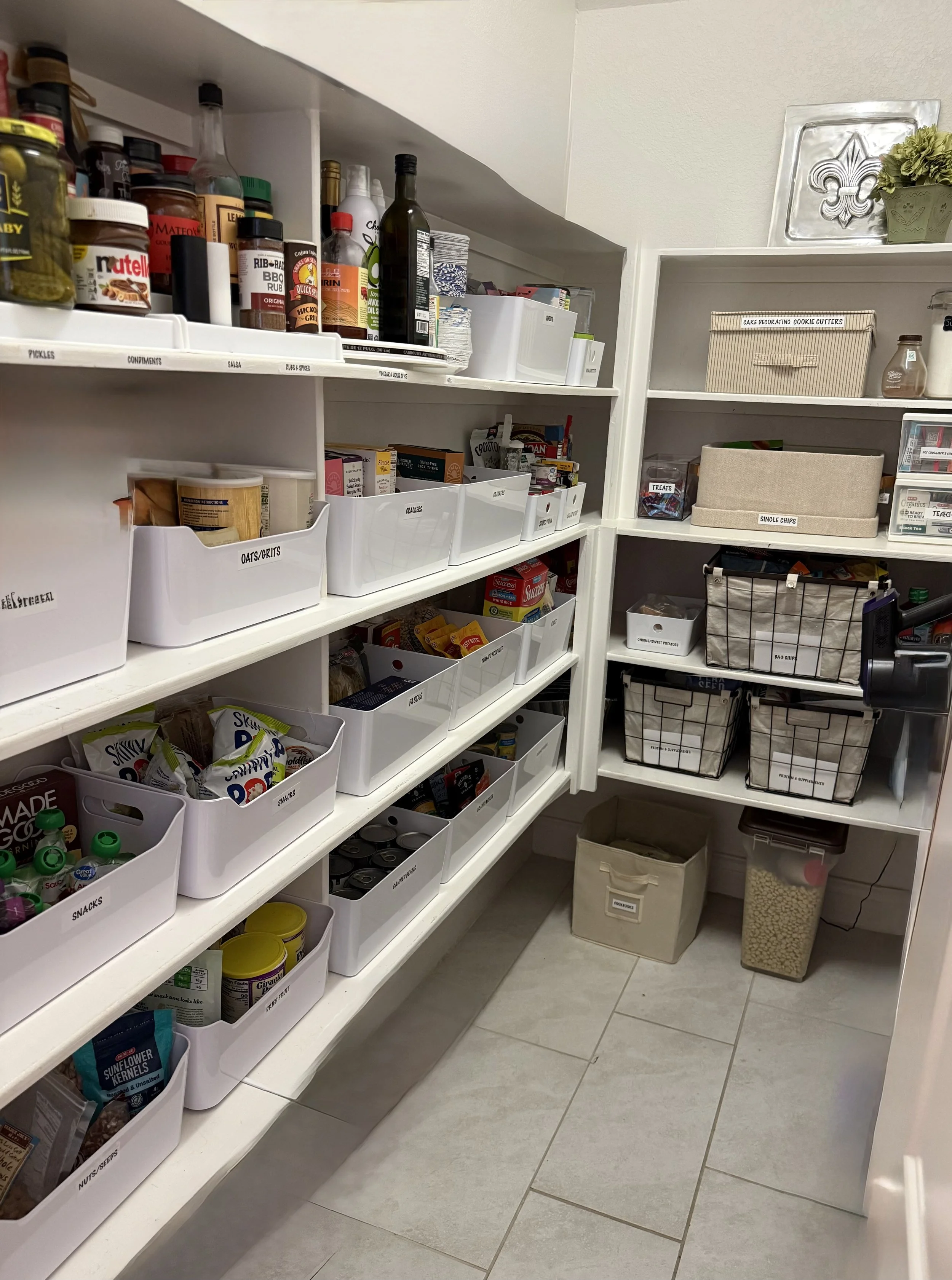 Luxury walk-in pantry professionally organized by Luxury Pro Organizer in Houston, Texas. White shelving features clearly labeled containers, arranged into easy to maintain categories creating a beautiful, function system for a busy family.
