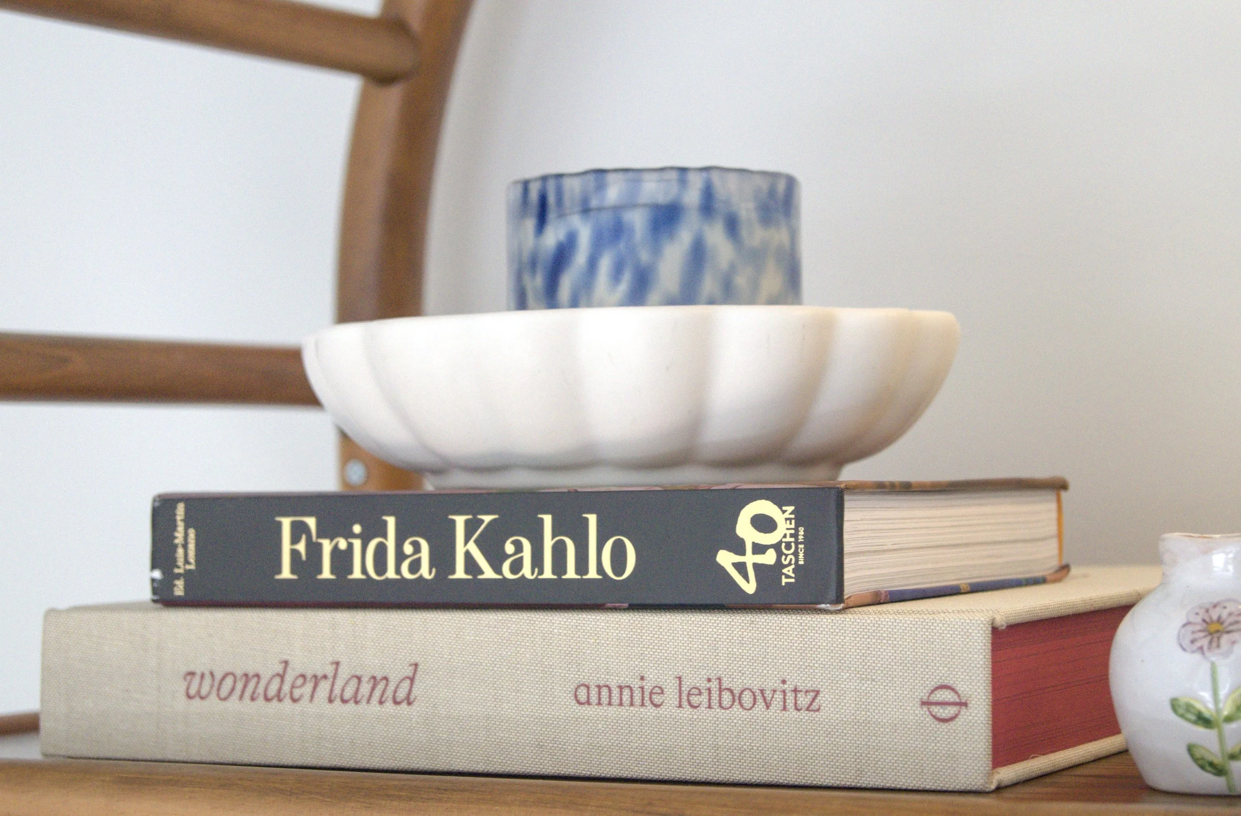 A stack of two books with decorative objects on top and to the side. The top book is titled "Frida Kahlo" and the bottom book is "wonderland" by Anne Leibovitz.