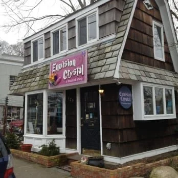 Small wooden shop with a sign reading "Envision Crystal" and decorative brick planters in front.