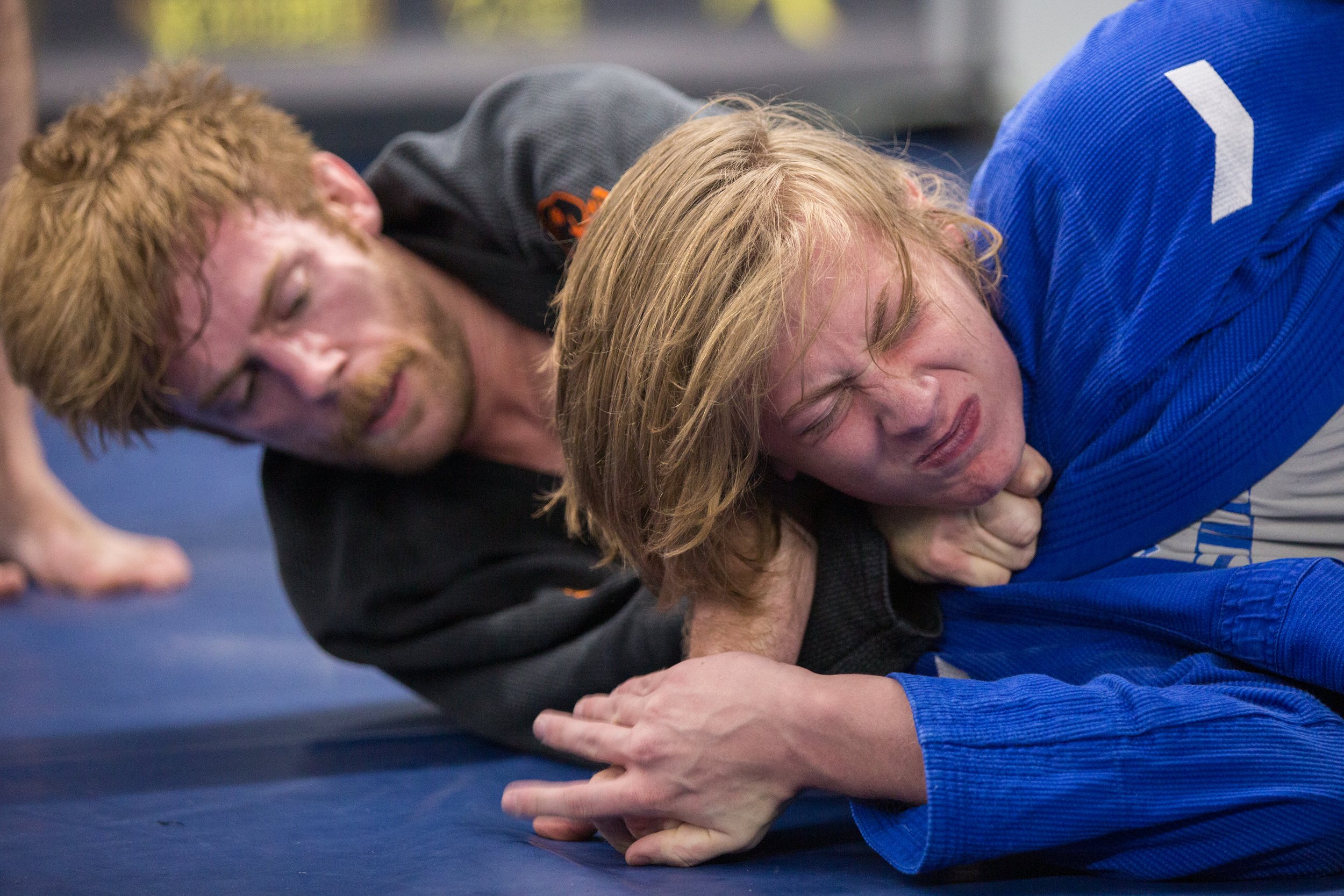 A Brazilian jiu-jitsu practitioner grimaces as he taps to a choke.