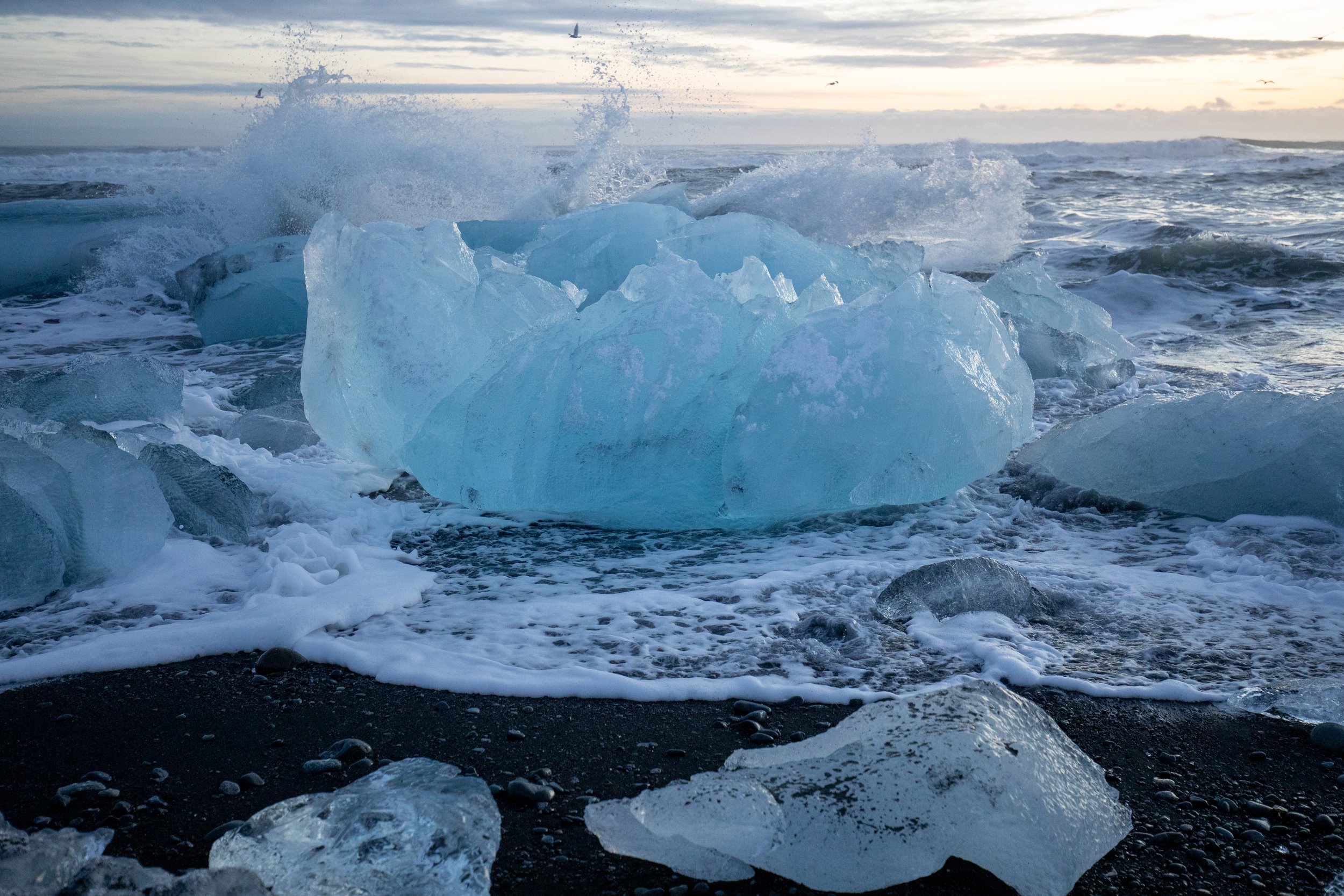 Waves crash over an ice boulder on Diamond Beach in Iceland.