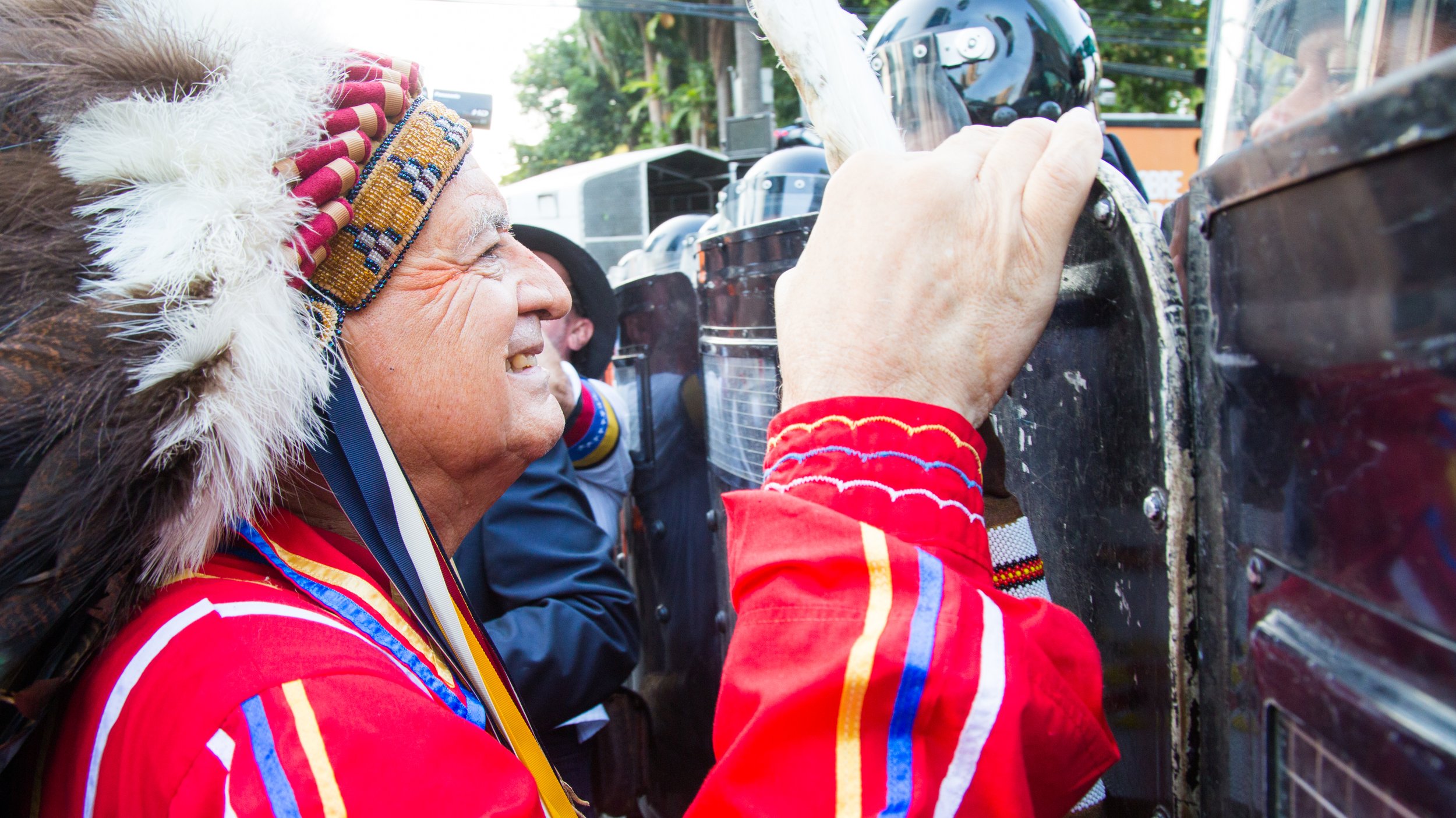 Chief Phil Lane, Jr. of the Ihanktowan Lakota and Chickasaw nations smiles at a riot officer during a demonstration against the exclusion of Indigenous peoples from the 2015 Summit of the Americas in Panama City, Panama.
