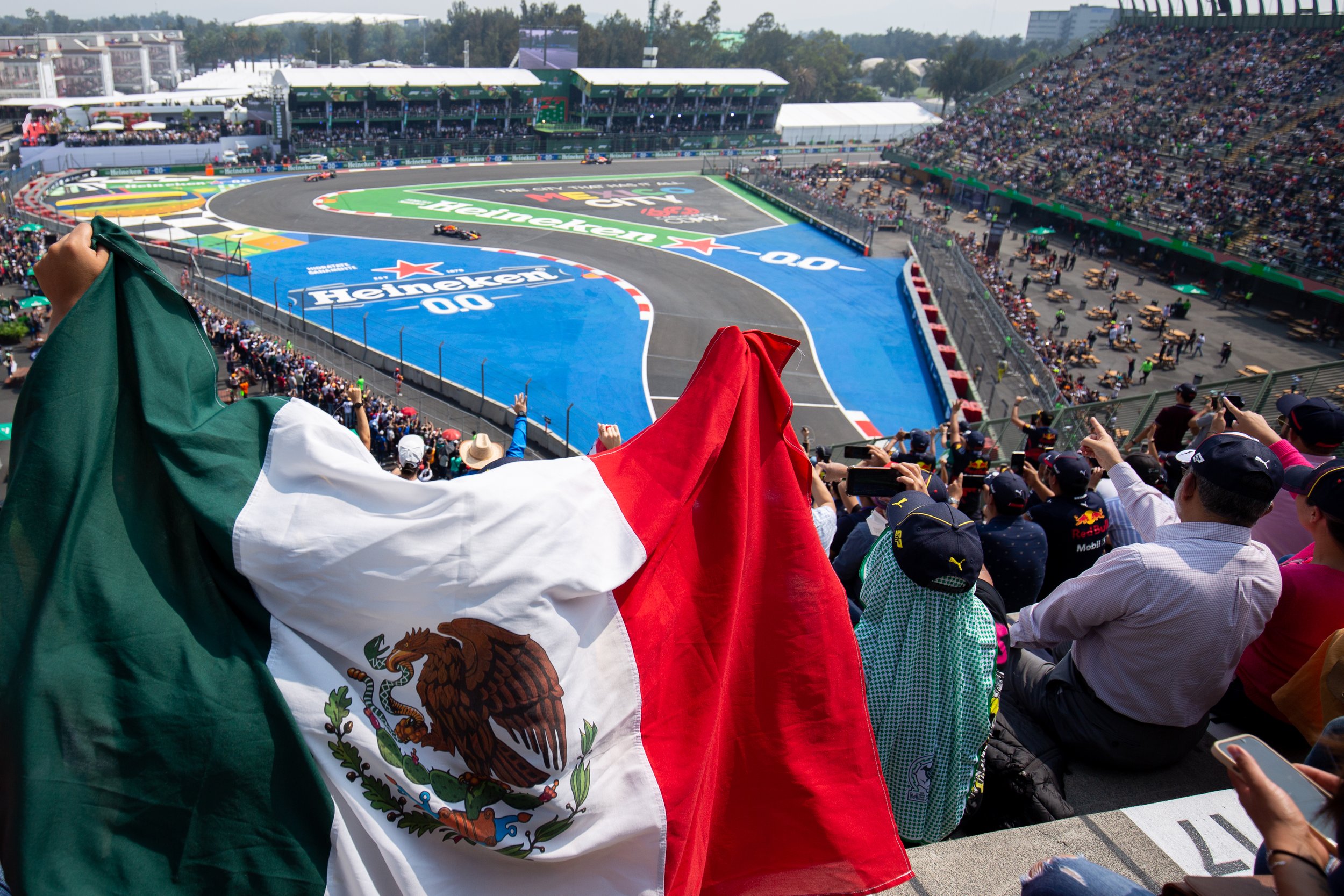 Fans wave a Mexican flag and gesture as Formula 1 driver Sergio "Checo" Pérez drives by at the 2022 Mexican Grand Prix.