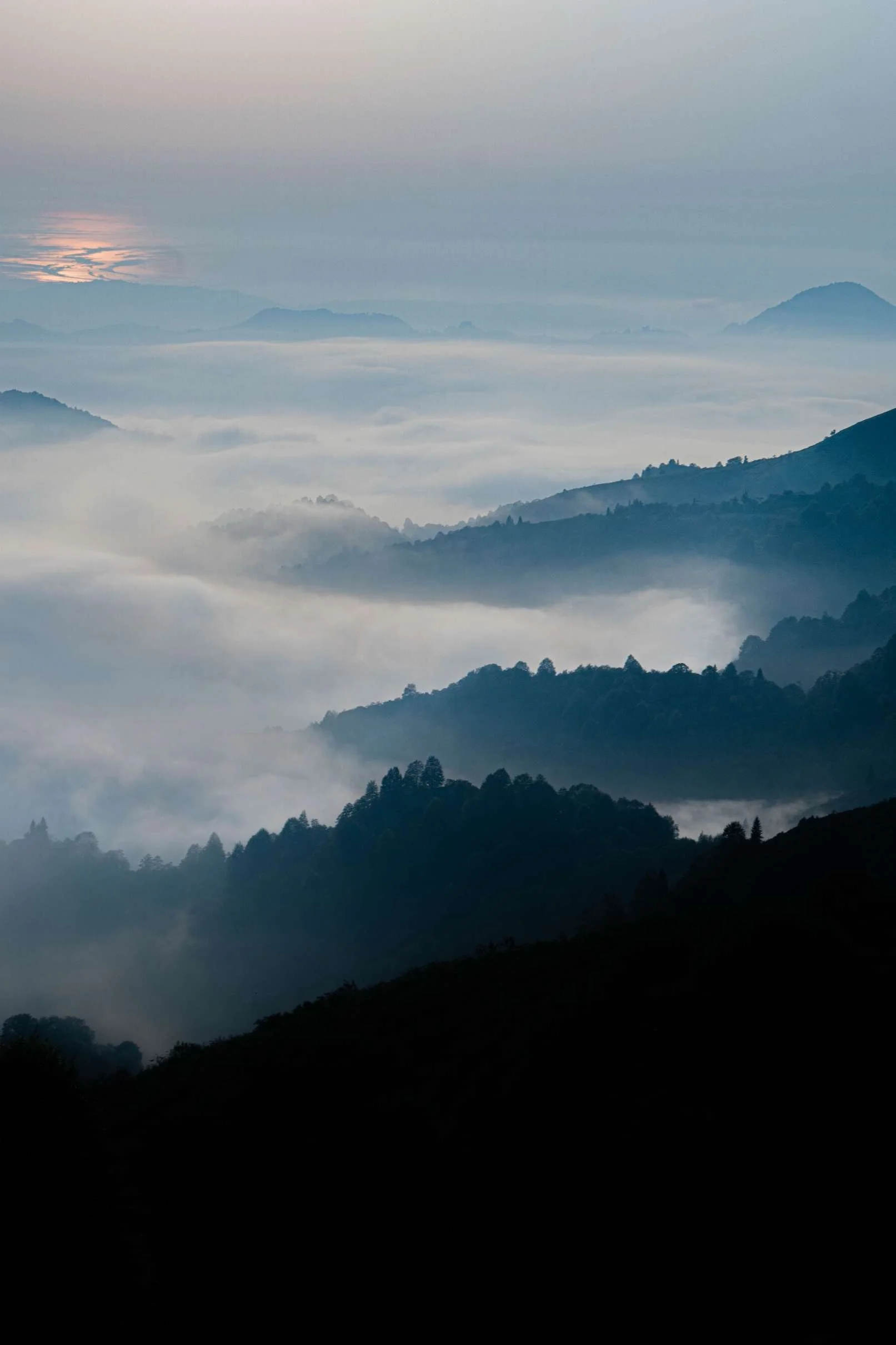 Scenic view of misty mountains and valleys at sunrise with a soft pink and blue sky.