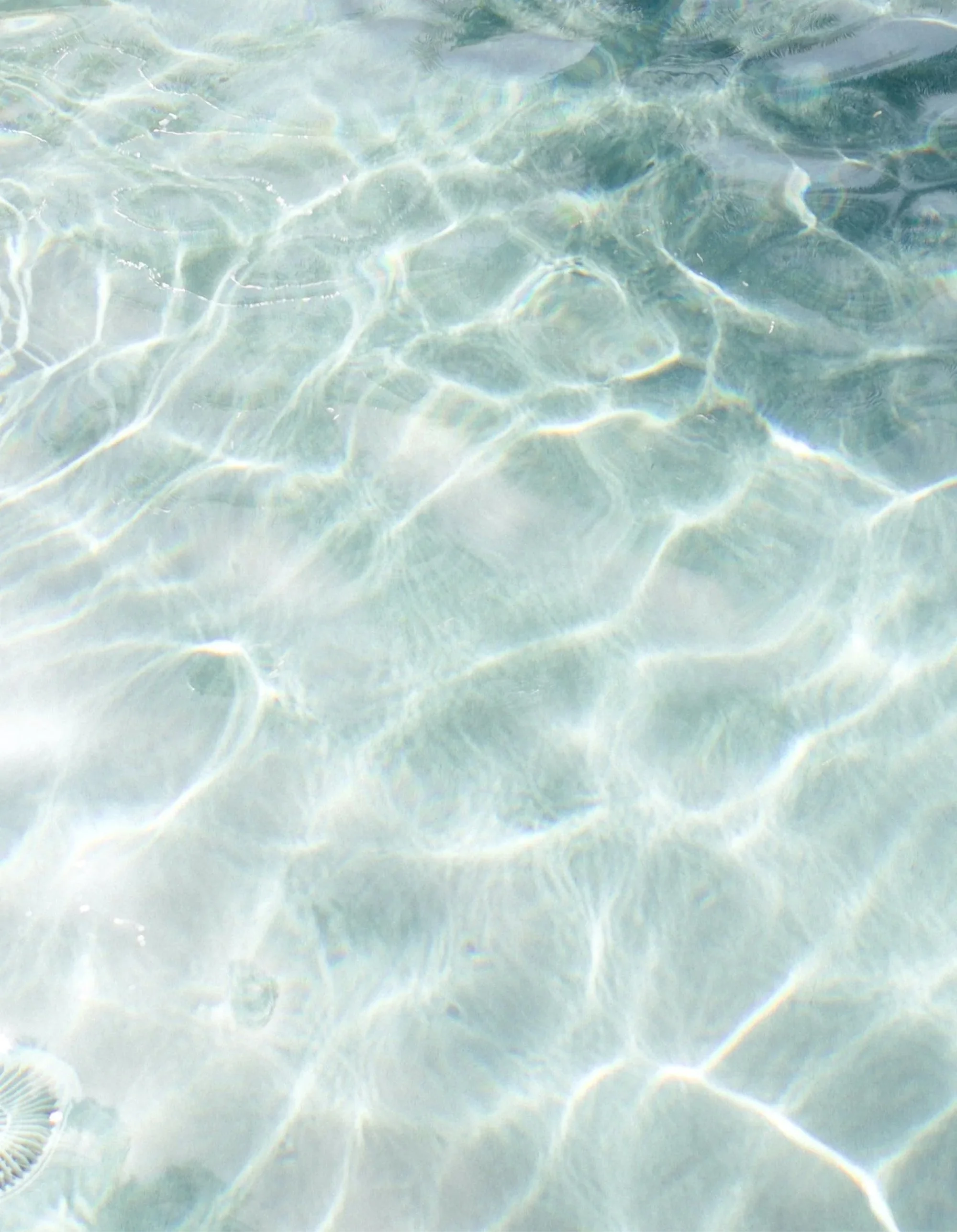 Close-up of clear, shallow water with sunlight creating reflections and patterns on the sandy bottom.