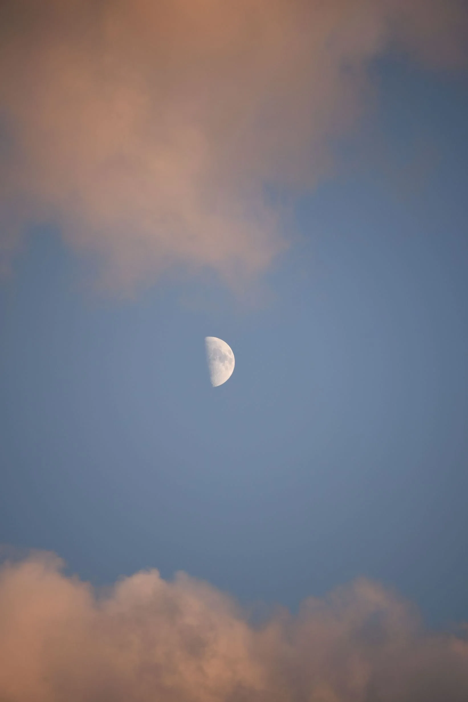 The image shows a waxing crescent moon in the sky with some orange and pink clouds at sunset or sunrise.