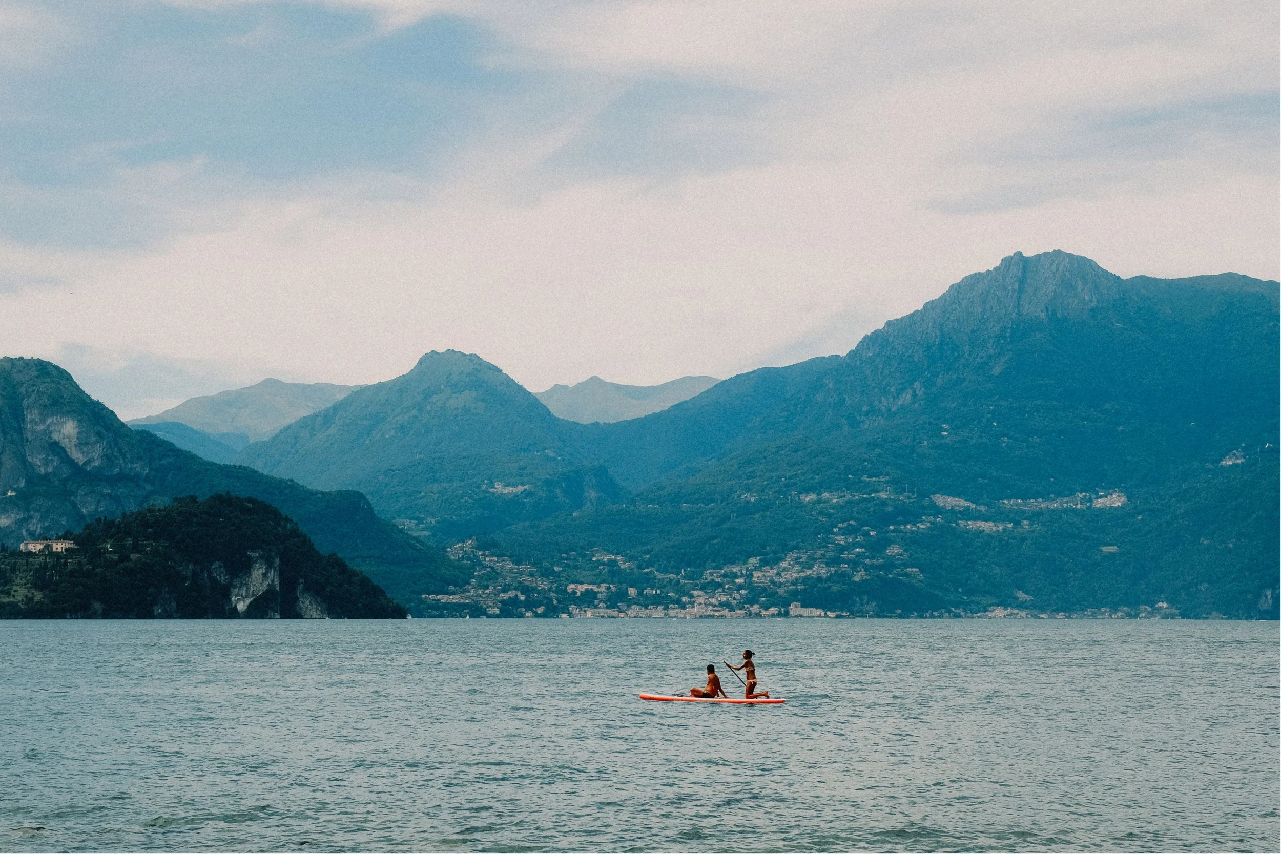Two children paddleboarding on a lake with mountains in the background.