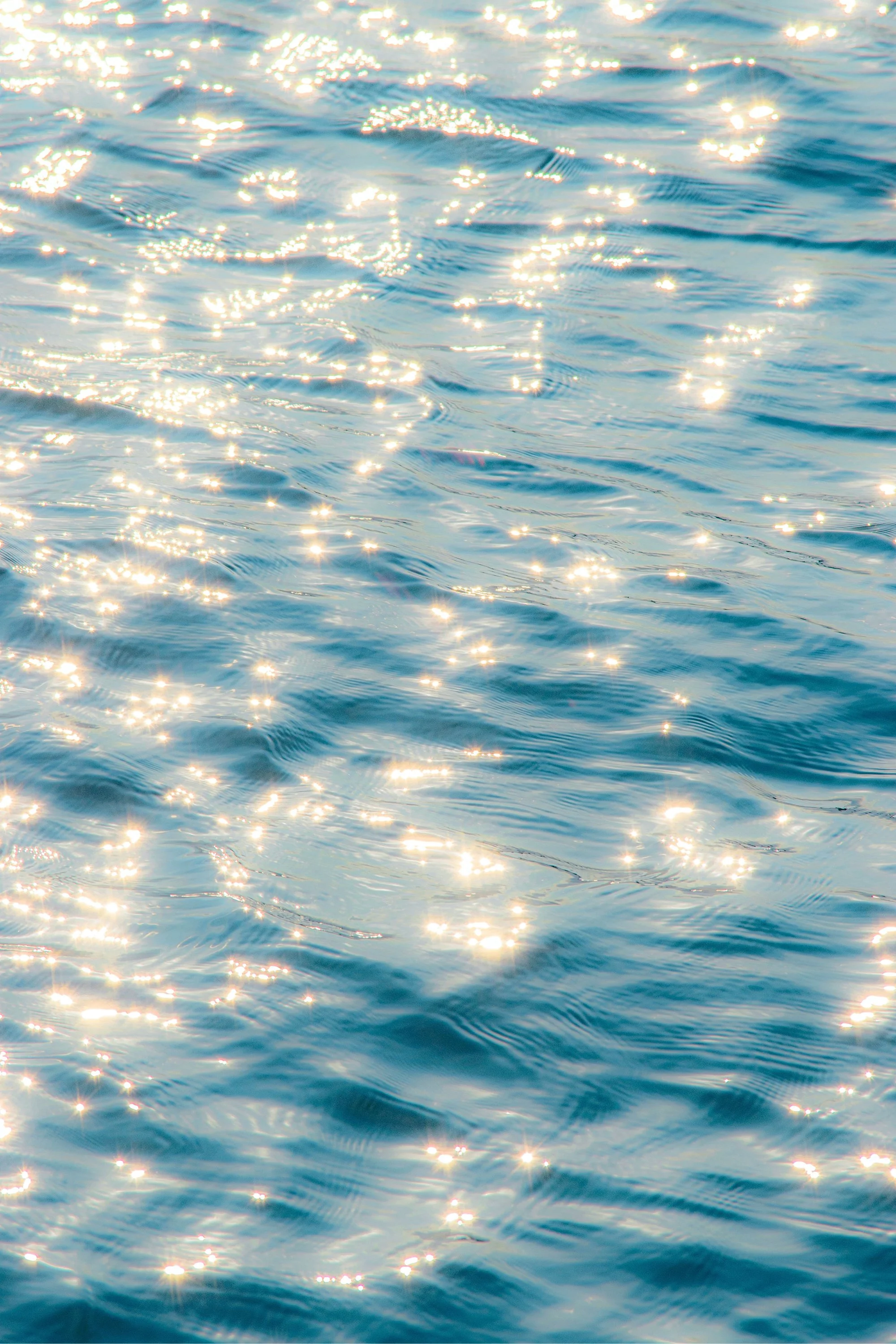 Sunlight reflecting on the surface of a blue body of water, creating bright sparkles and gentle ripples.