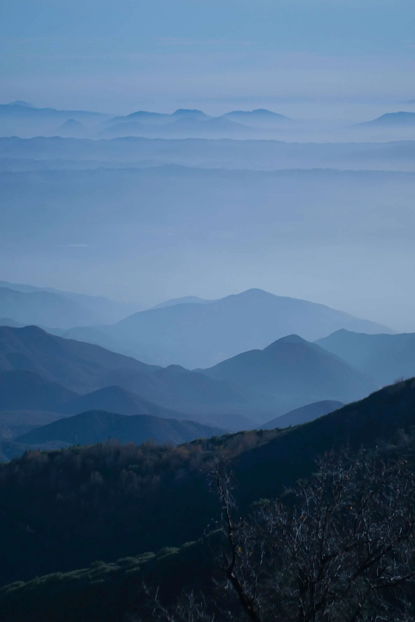 Multiple mountain ridges in various shades of blue fading into the distance under a clear blue sky.