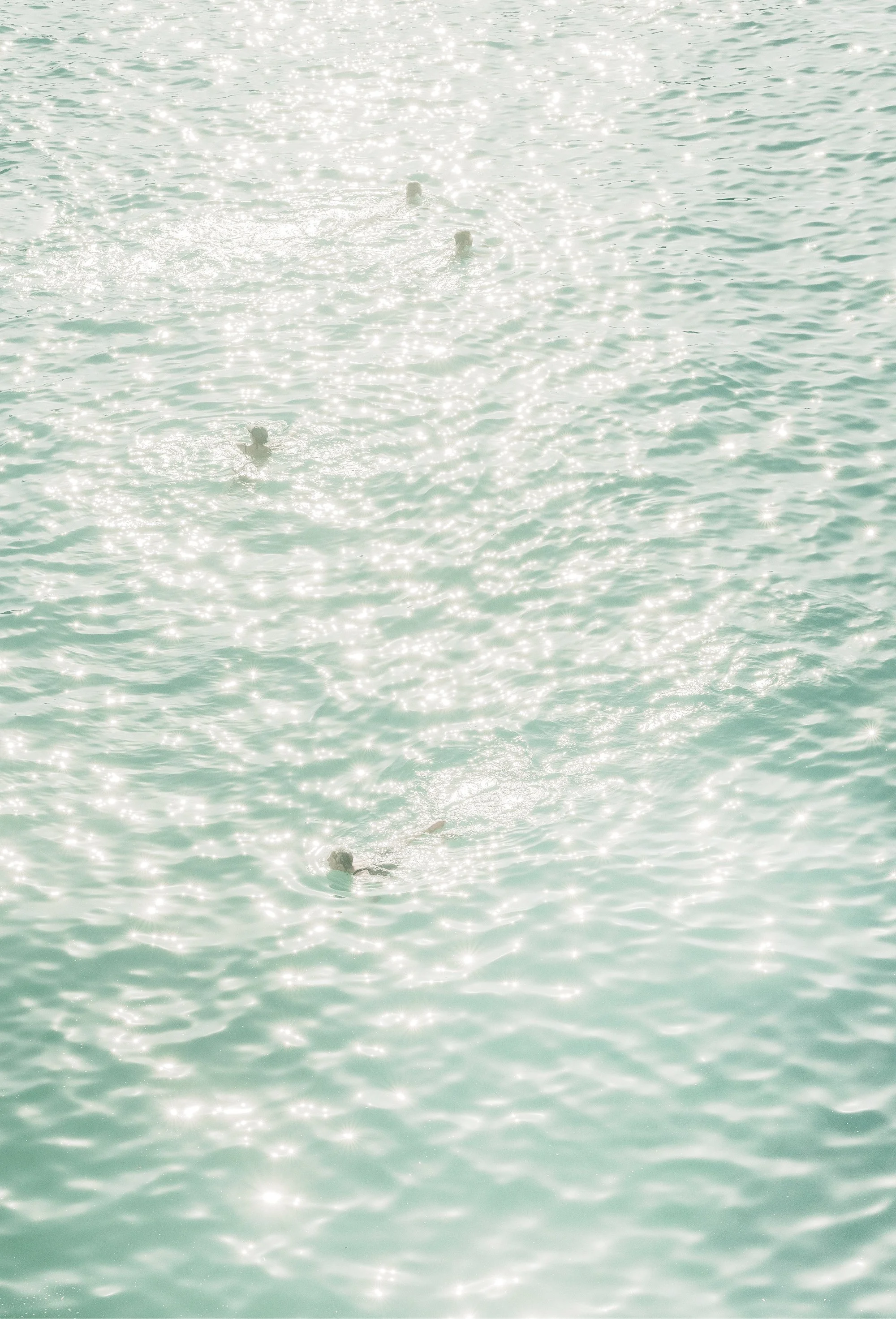 People swimming in the ocean with sunlight reflecting on the water's surface.