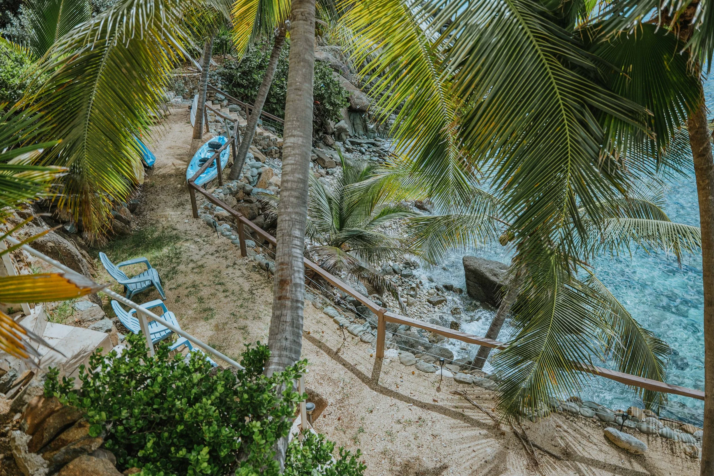Sandy pathway with Adirondack chairs and kayaks overlooking a rocky beach on Magens Bay
