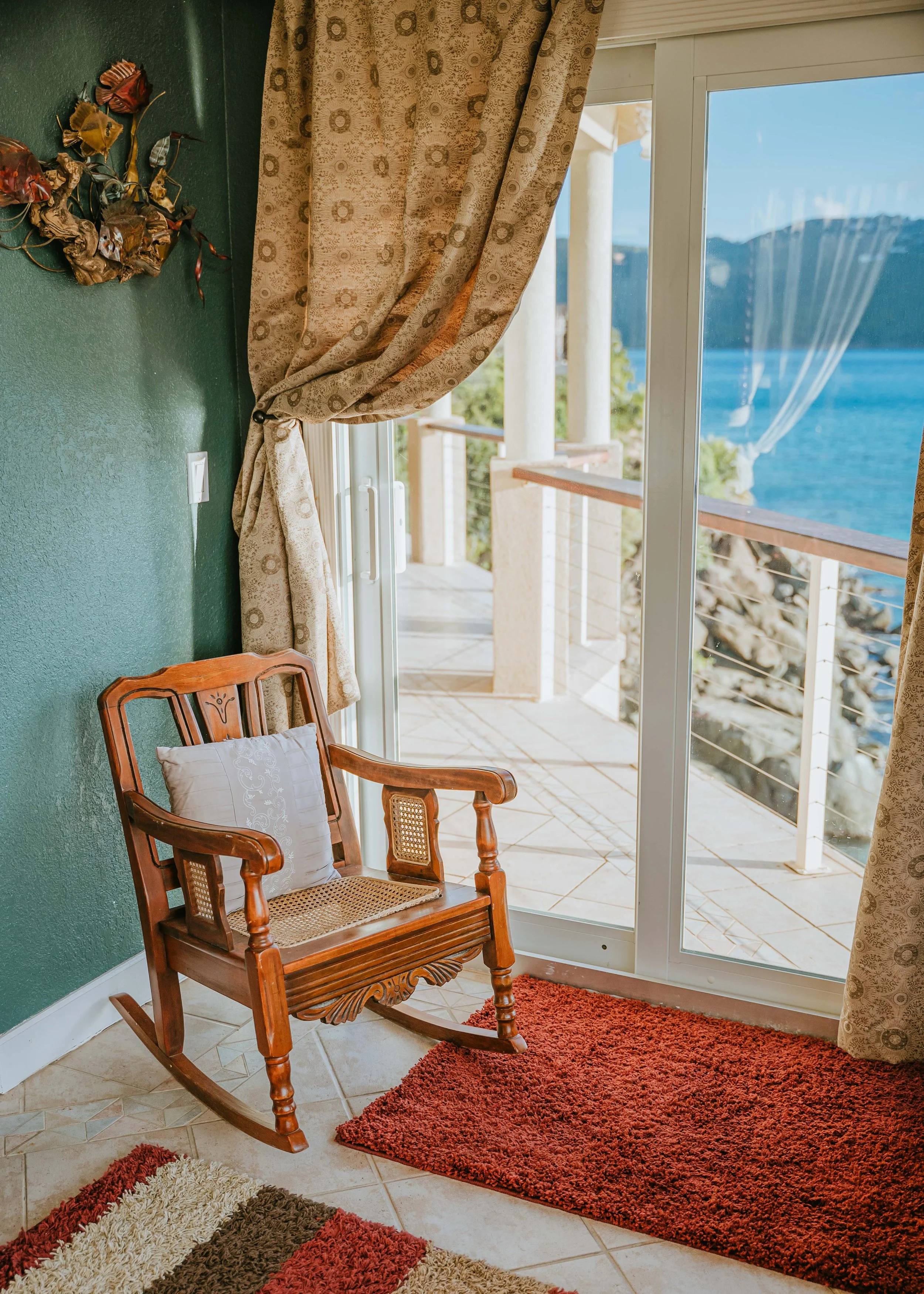 Rocking chair next to sliding glass door through which the upper veranda and eastern end of Magens Bay can be seen