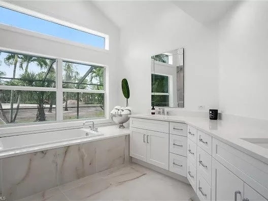 Bright bathroom with white cabinetry, a large window, and a view of palm trees outside