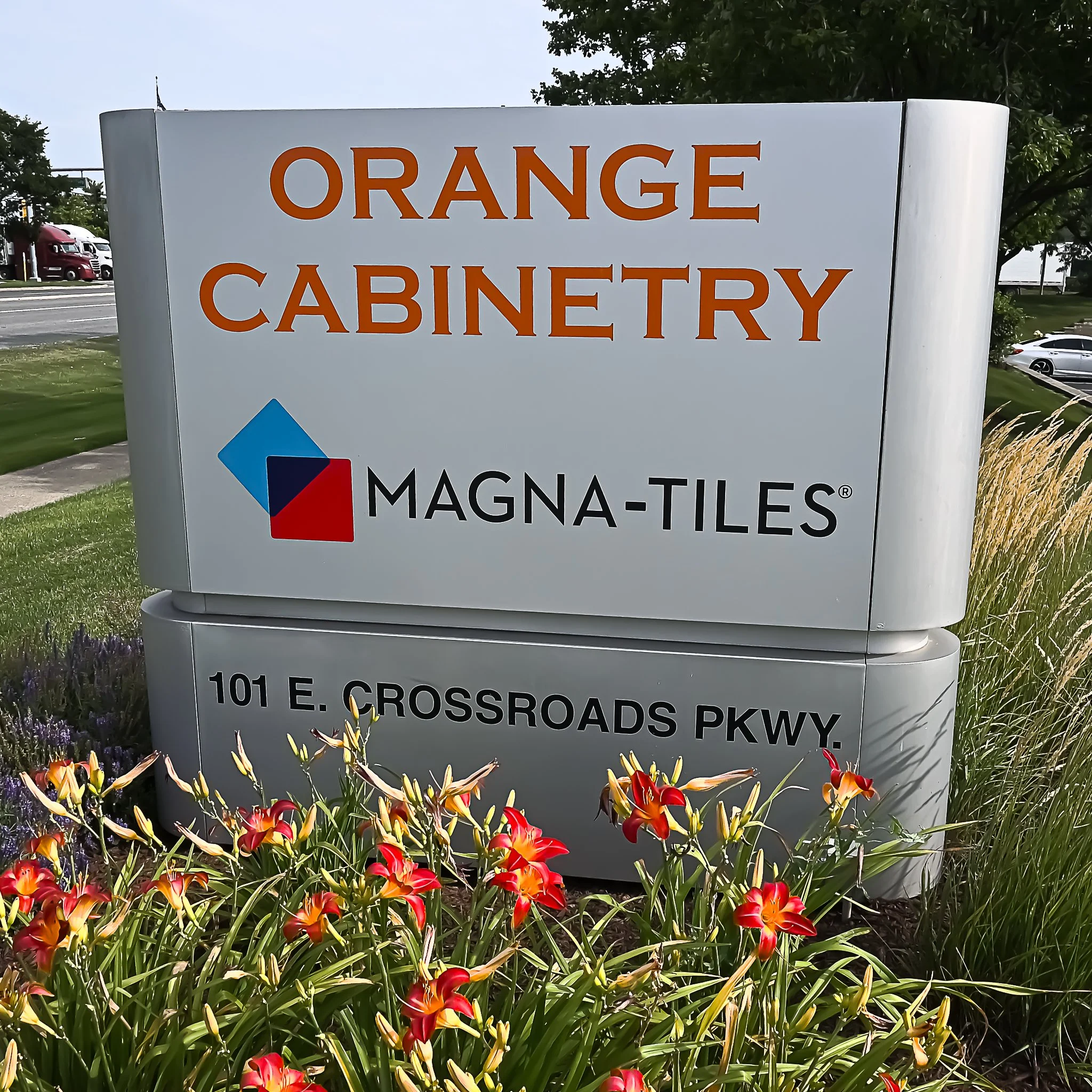 Outdoor sign for Orange Cabinetry at 101 E. Crossroads Parkway, surrounded by flowers and greenery.