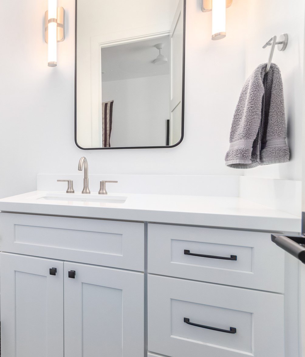 Clean white bathroom vanity with a rectangular mirror, gray towel hanging on a hook, and modern light fixtures on the wall.