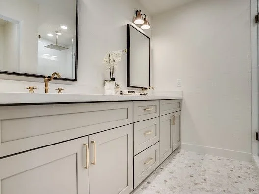 Bathroom vanity with gray cabinets, two mirrors, a flower vase, and lighting fixtures.