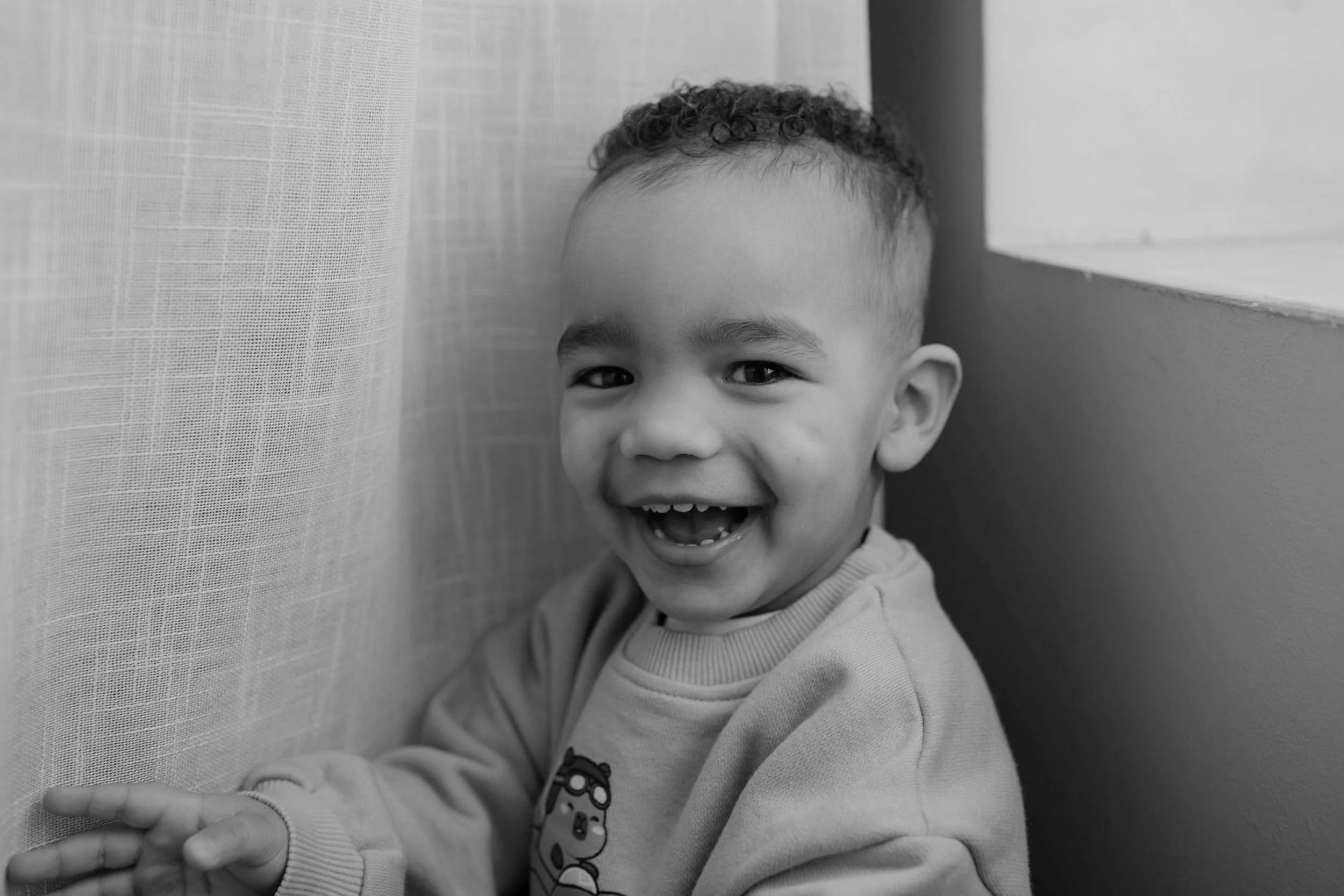 little boy smiling really big at the camera from behind a curtain at a Lebanon, TN photography studio