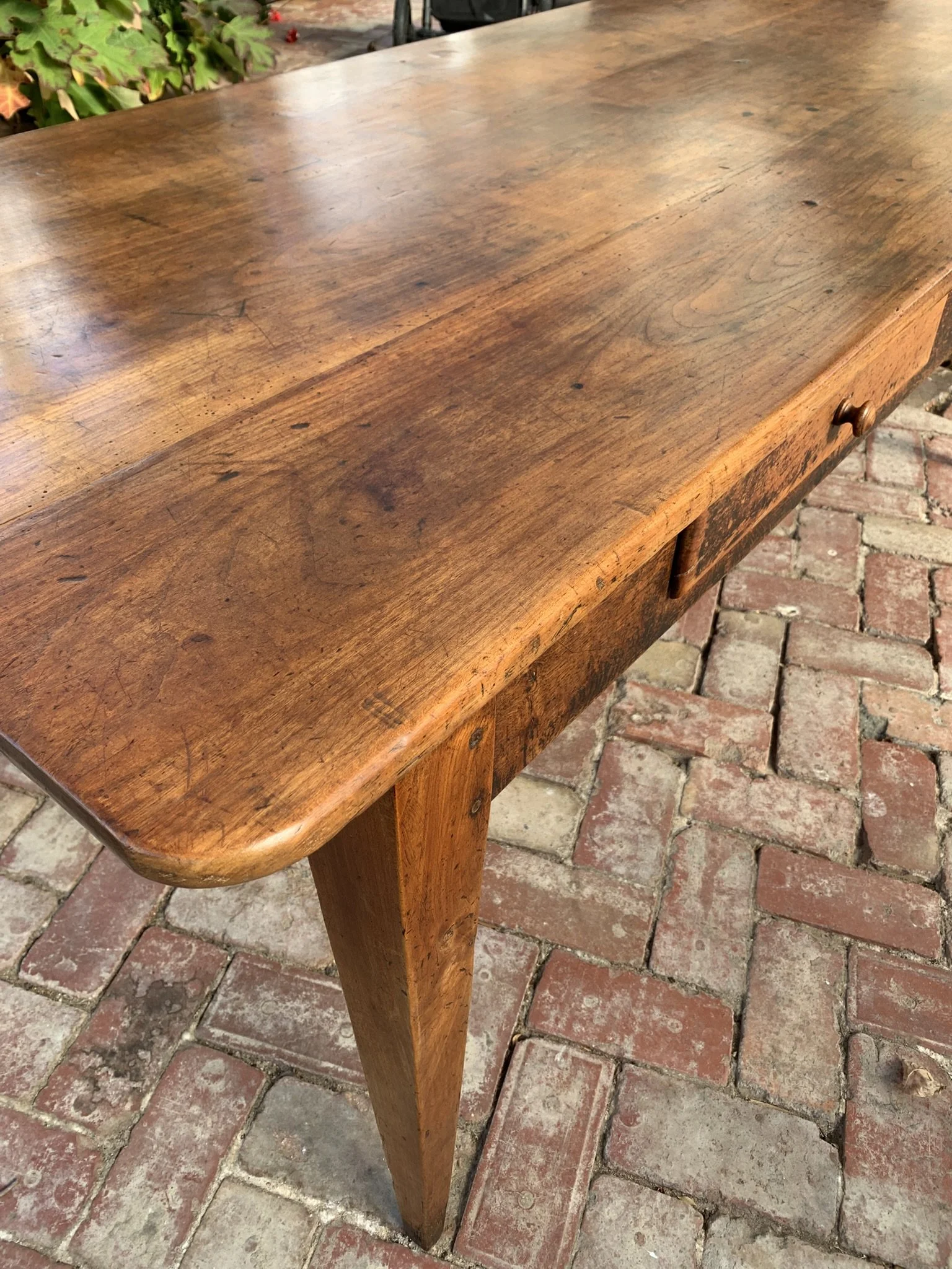 Close up of cherry wood table top showing patina, frieze drawer with turned wood knob and dovetail joinery