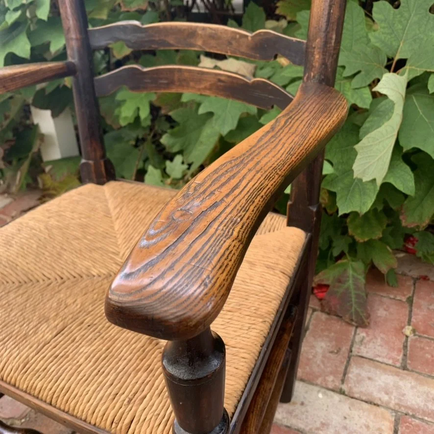 Close-up profile view of the wide, sweeping right armrest, showcasing the smooth historic wear and deep wood grain contrast.