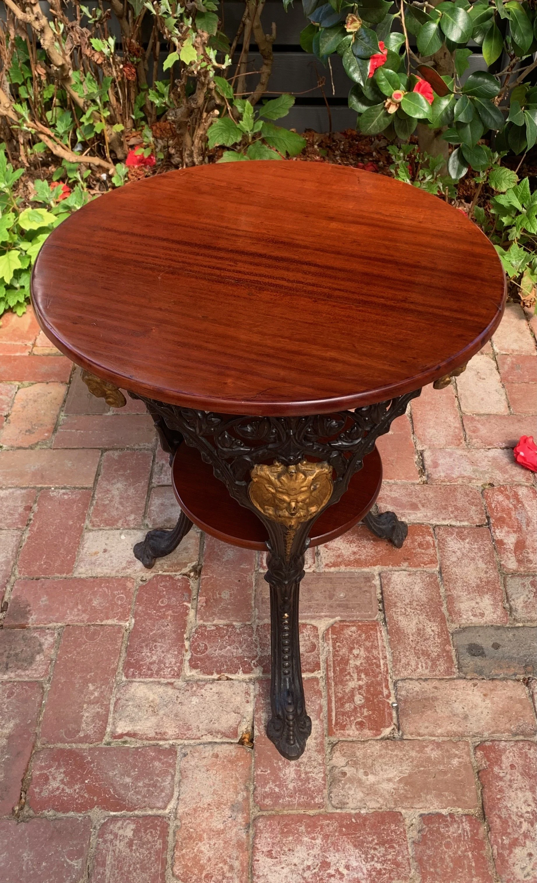 Circa 1920 cast iron and mahogany pub table, tripod cabriole legs, paw feet, gilded Bacchus mask medallion