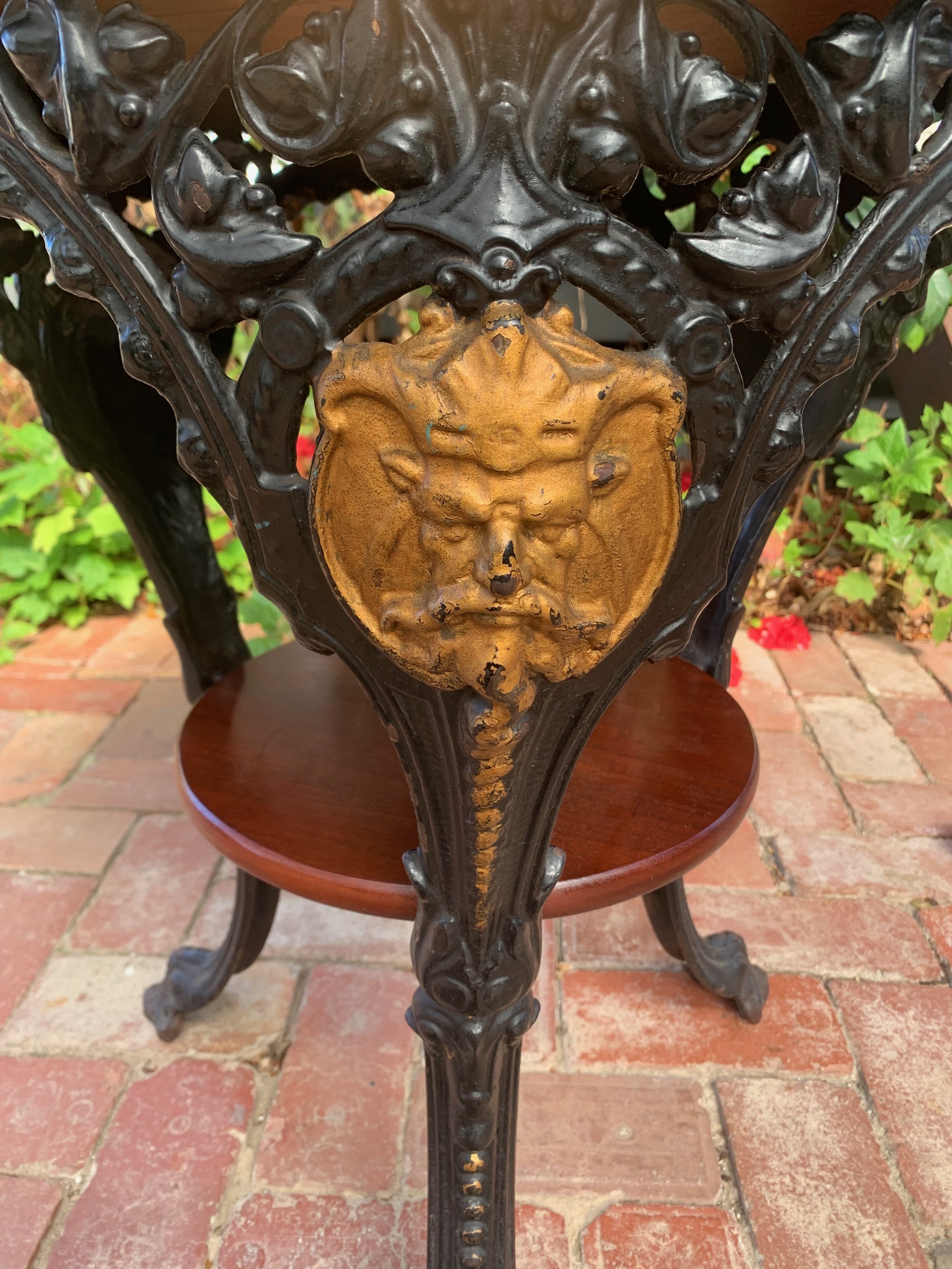 Circa 1920 cast iron and mahogany pub table, tripod cabriole legs, paw feet, gilded Bacchus mask medallion