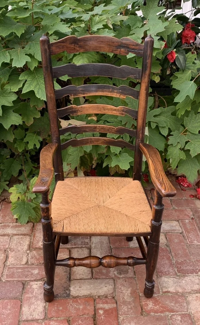 Straight-on front view of the antique English country chair, displaying the symmetry of the 6-ladder back, the rush seat, and the lower turned stretchers.