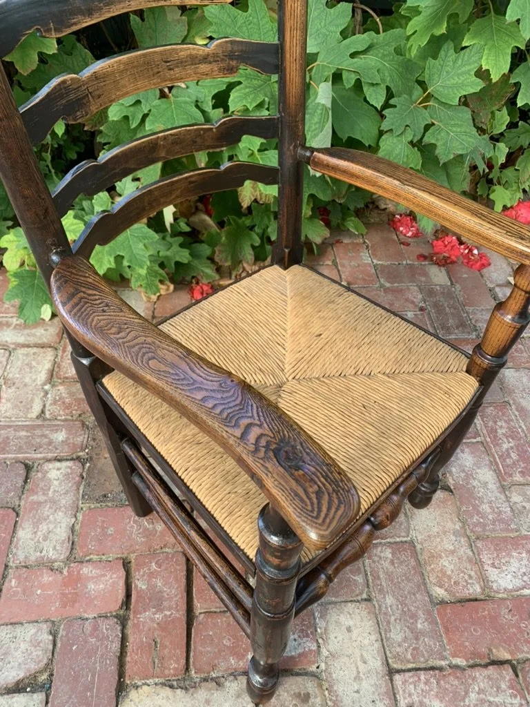 Overhead angled view focusing on the tightly woven natural rush seat and its connection to the sculpted oak arm and turned support posts.