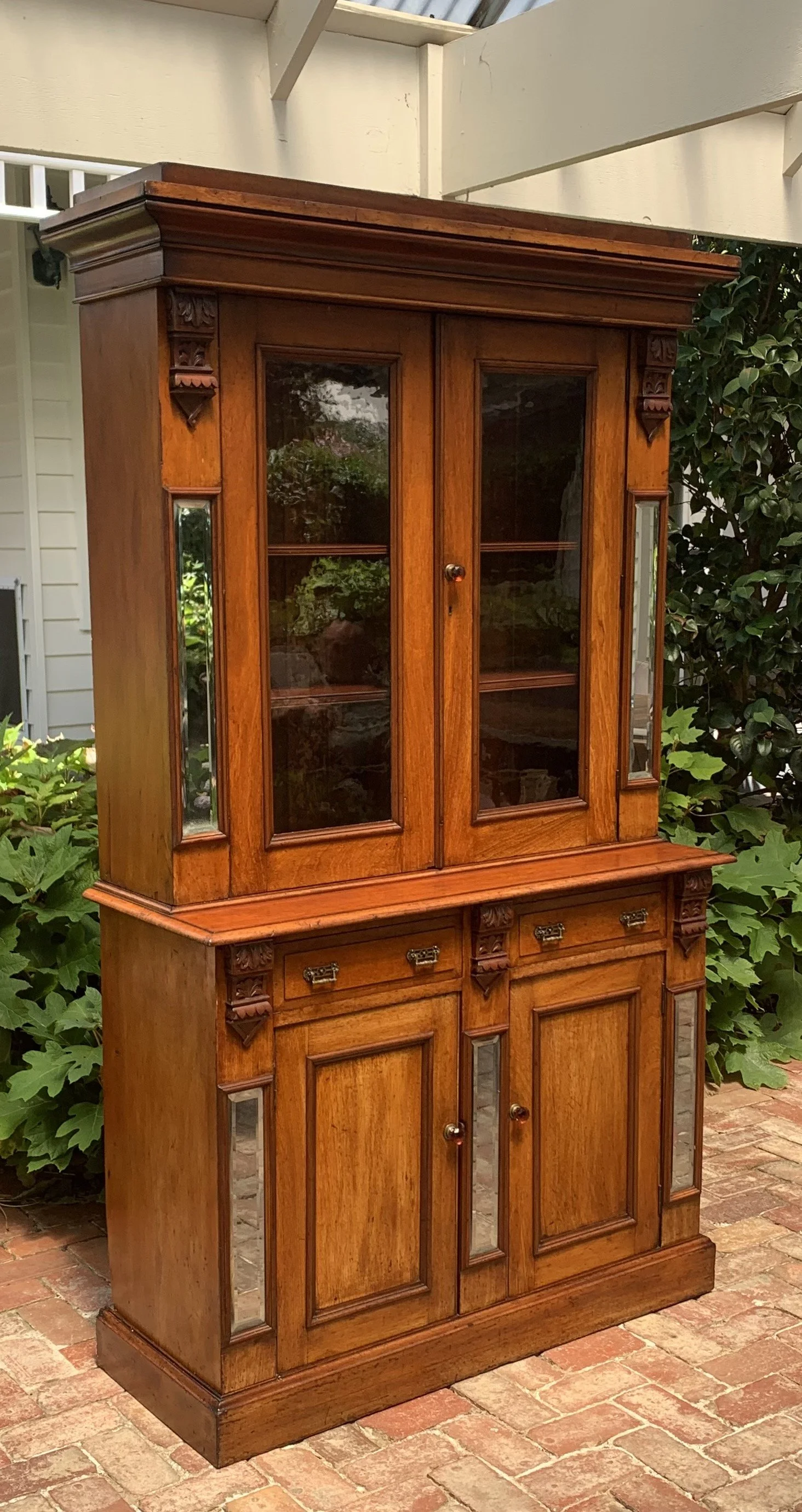 Antique Australian cedar Victorian bookcase circa 1890 with glazed upper cabinet, beveled mirror panels, carved corbels and original amber glass knobs