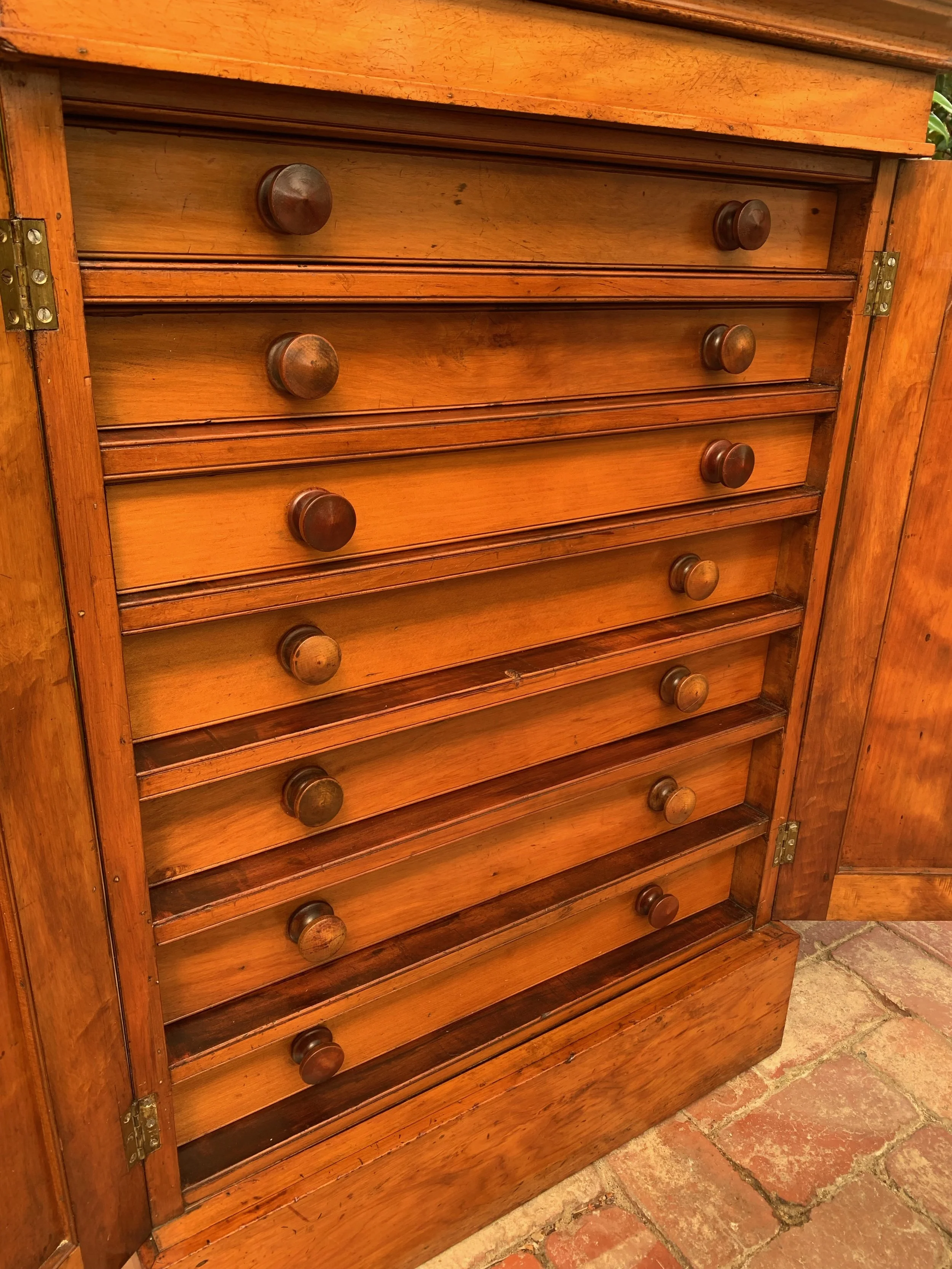 Close up view of antique collectors cabinet with doors open revealing bank of graduating drawers angled view