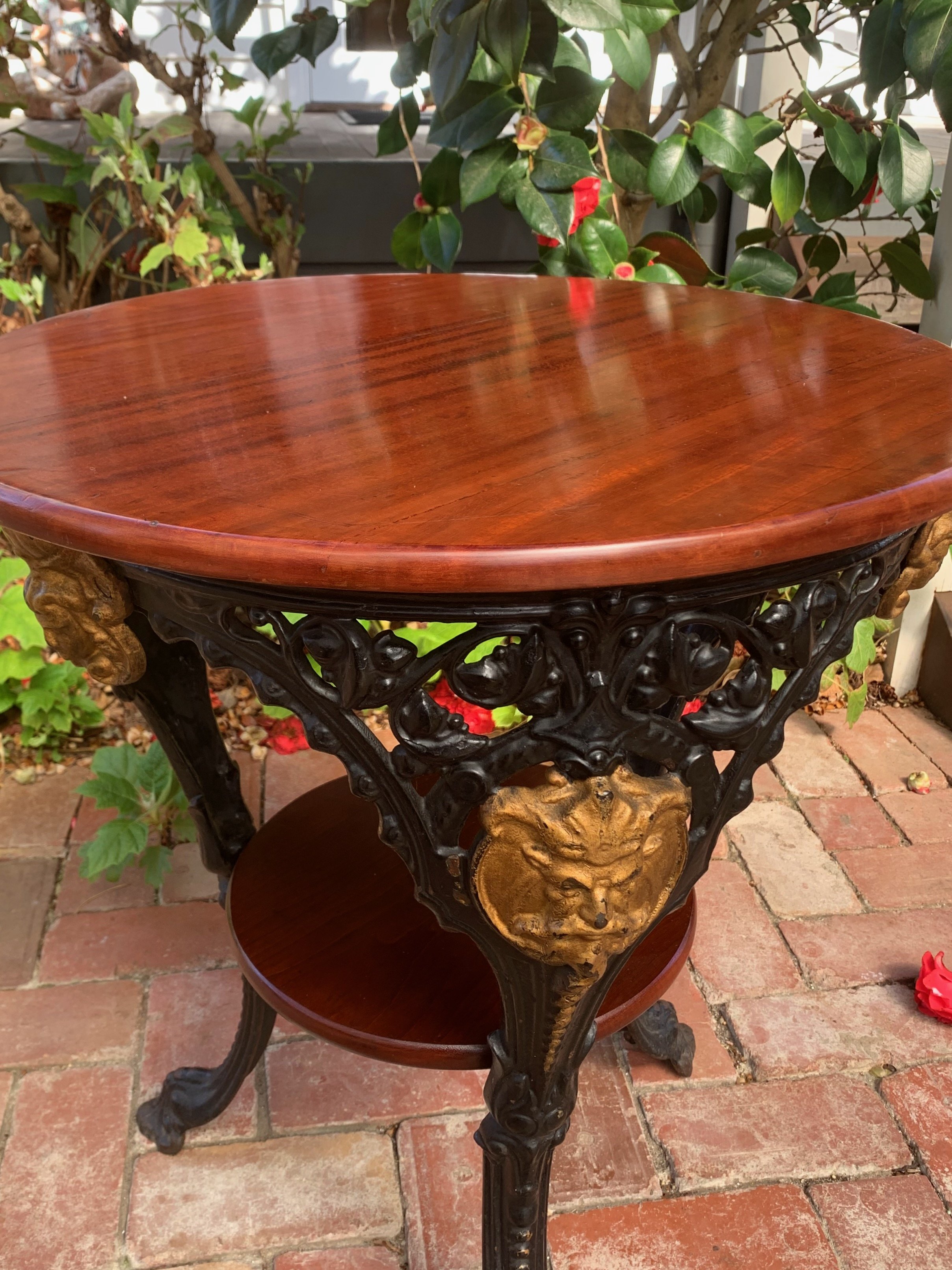 Early 20th century cast iron bistro table, C.1920, mahogany top grain detail, pierced tripod base, gilt mask