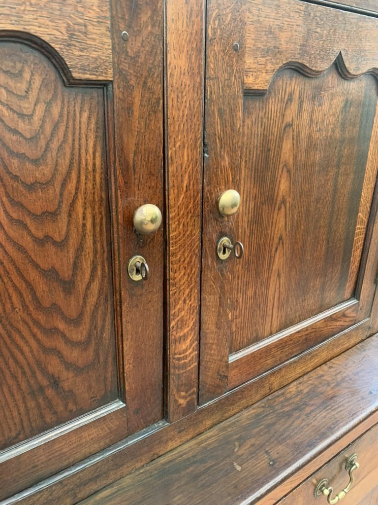 Close-up of Welsh oak cwpwrdd deuddarn cupboard doors, brass knob handles, working locks and scalloped panel tops
