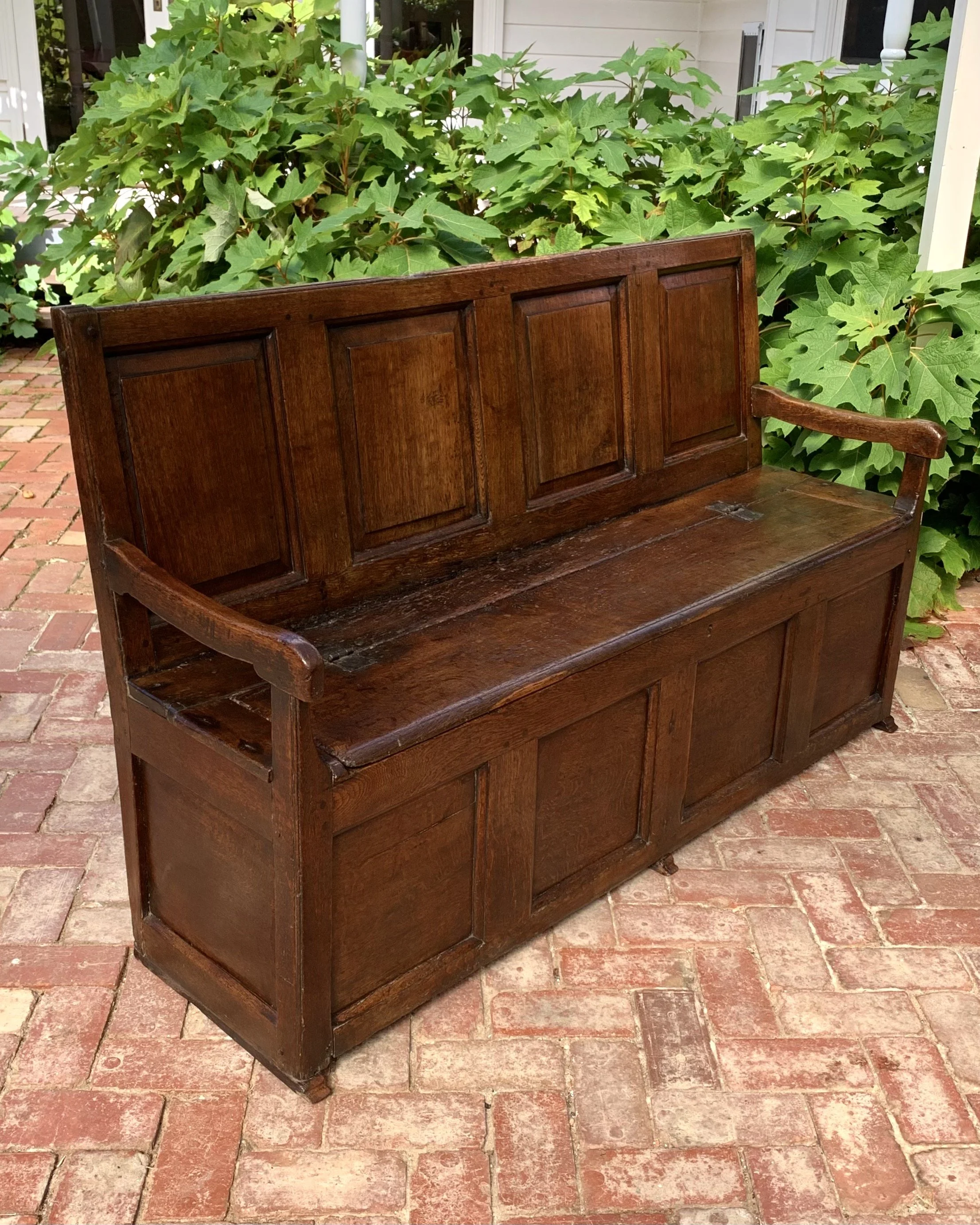 Angled view of antique welsh oak box settle with panelled back and lift-up seat c.1720