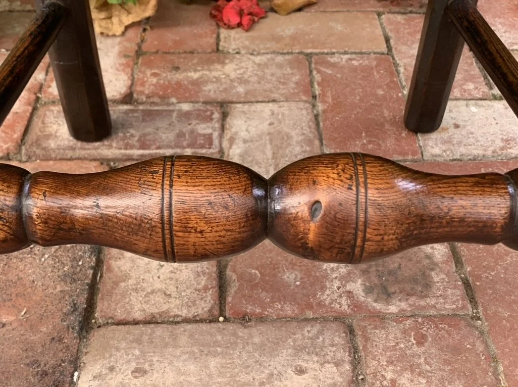 Macro detail shot of the deeply patinated, double-bulb turned timber front stretcher on the Georgian-era country chair.
