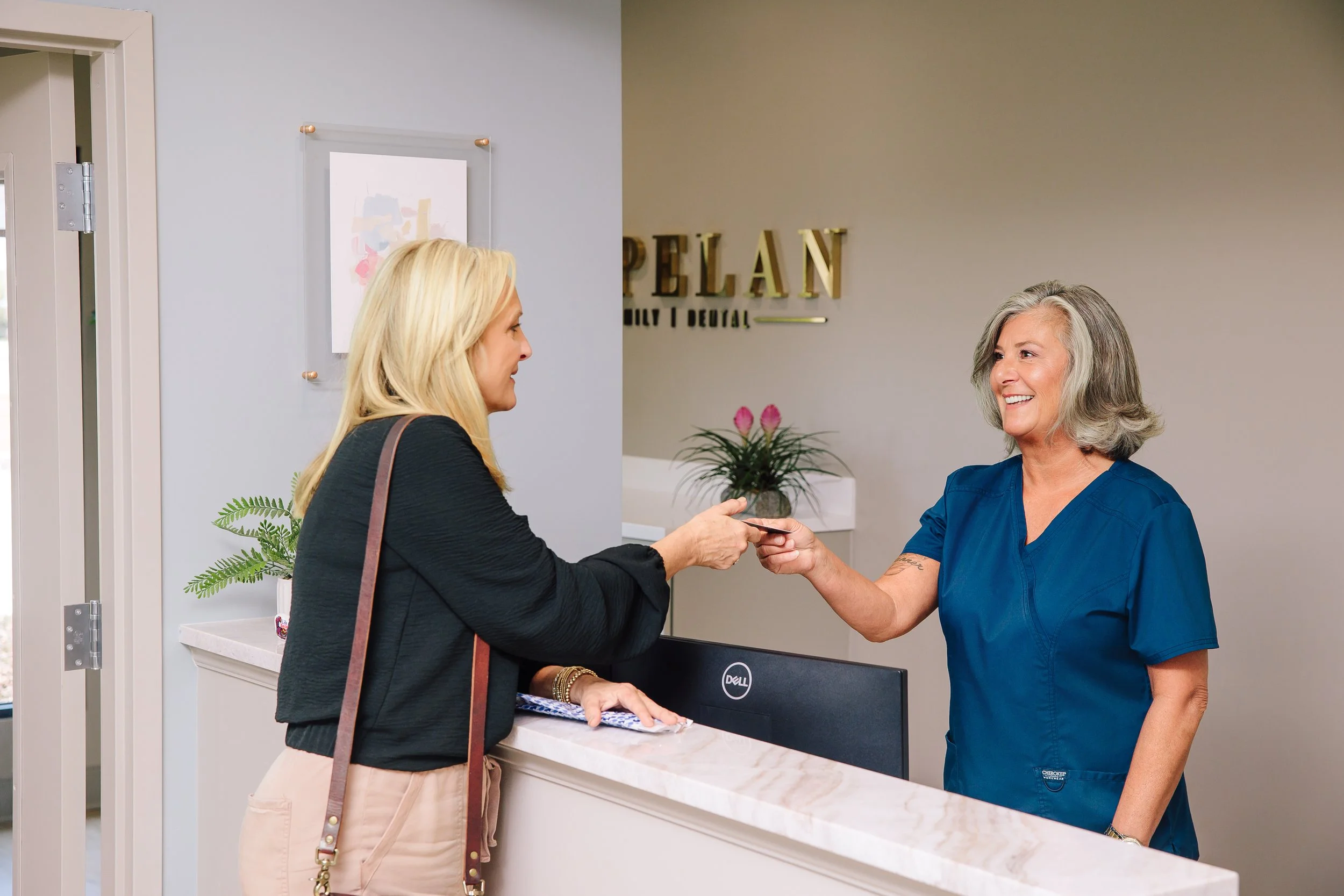 A cosmetic dental patient is handing payment to a smiling, friendly dental receptionist in a welcoming dental office.