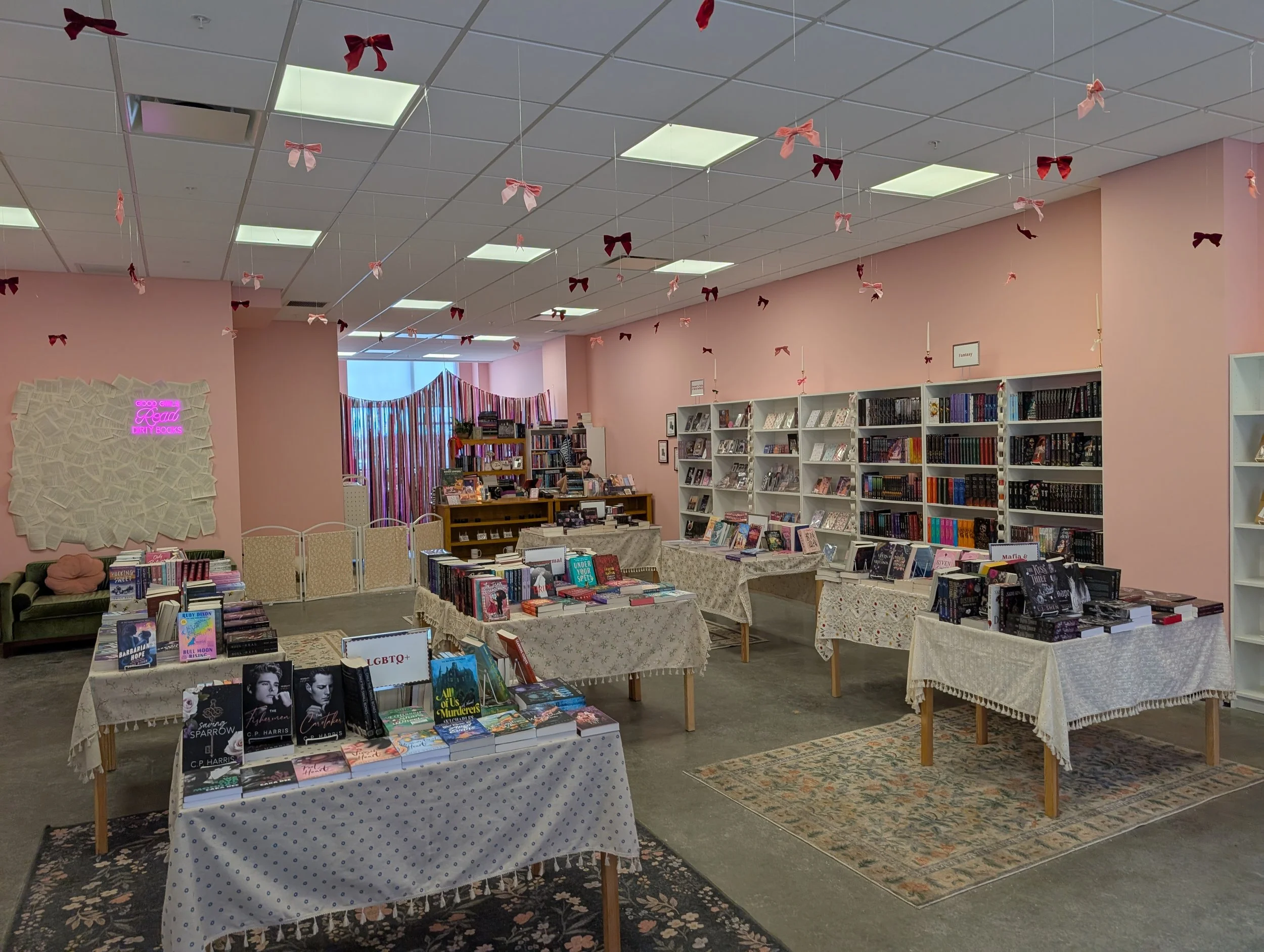 Spacious room with concrete floor, walls lined with stocked white bookshelves and low tables covered in piles of new books