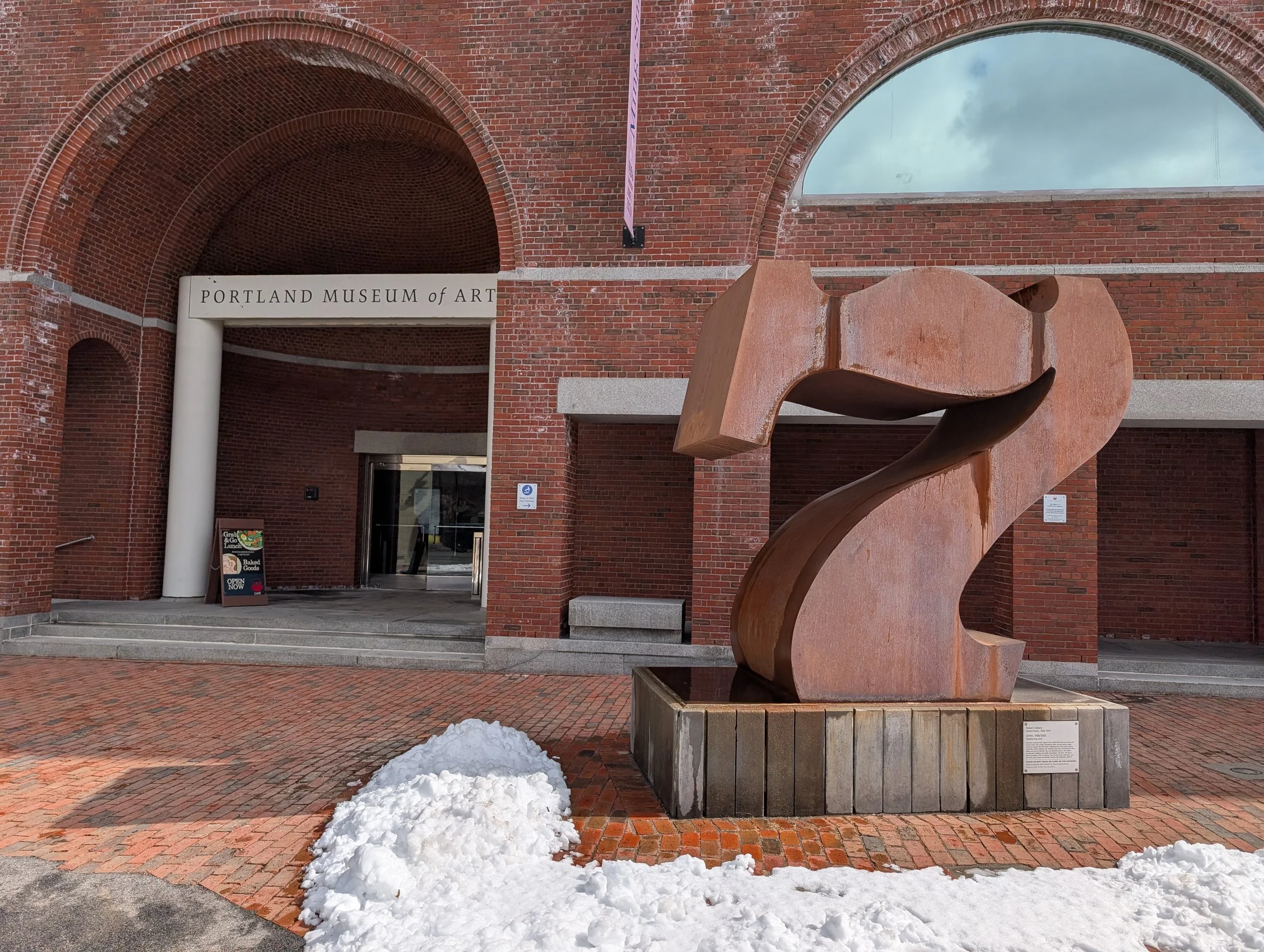 Modernist brick facade with a large, recessed, domed entry, and a rusty sculpture out front in the shape of a 7