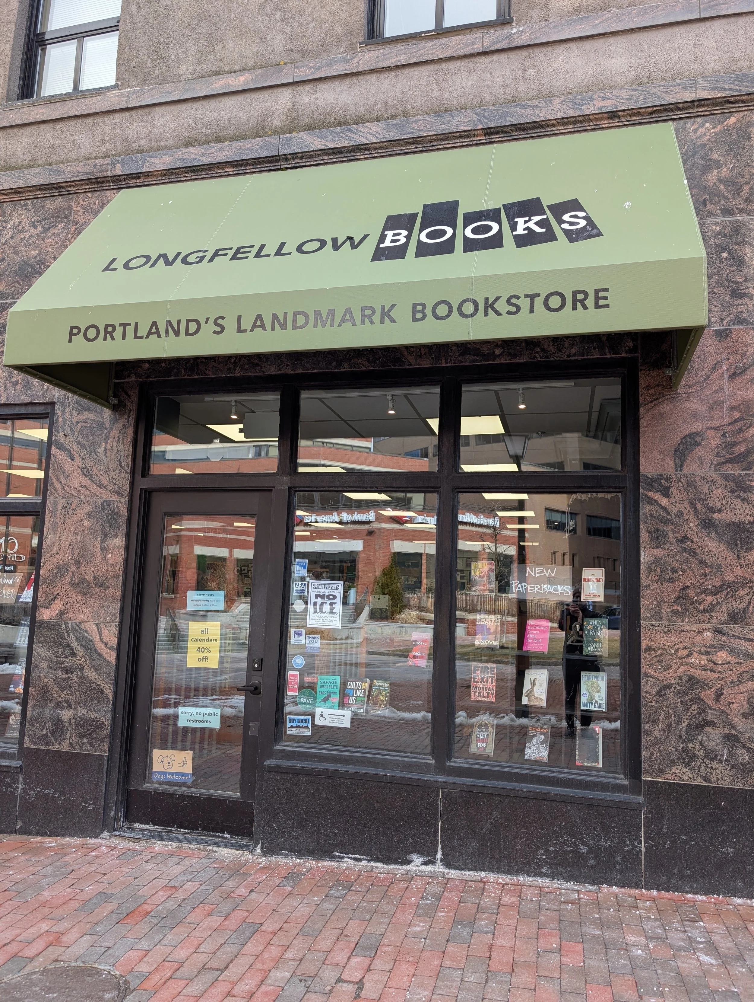Glass windows and door set into a marble storefront with an awning above bearing the company logo