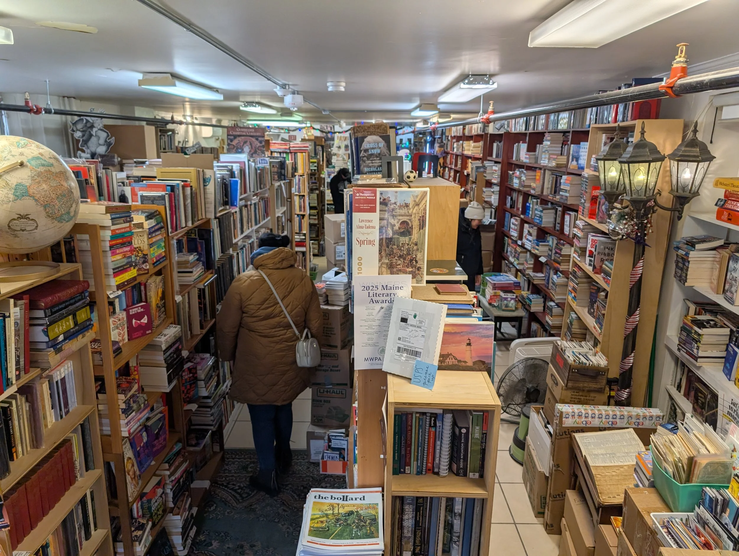 Multiple, narrow aisles defined by crammed bookshelves, and a figure in winter coat and hat walking down one of the aisles