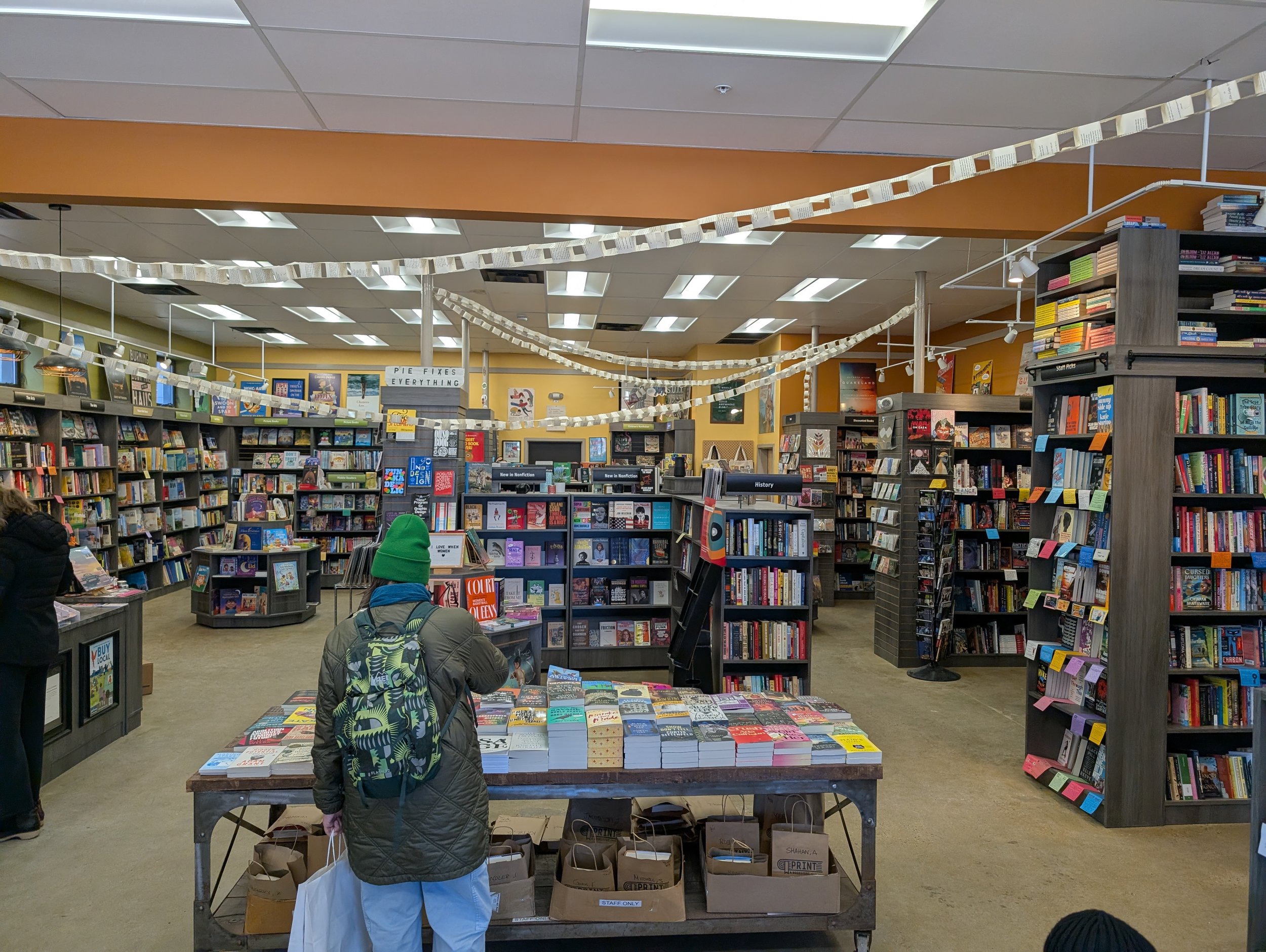 Airy, modern room with a concrete floor, stocked bookshelves, and a low table covered with stacks of new books