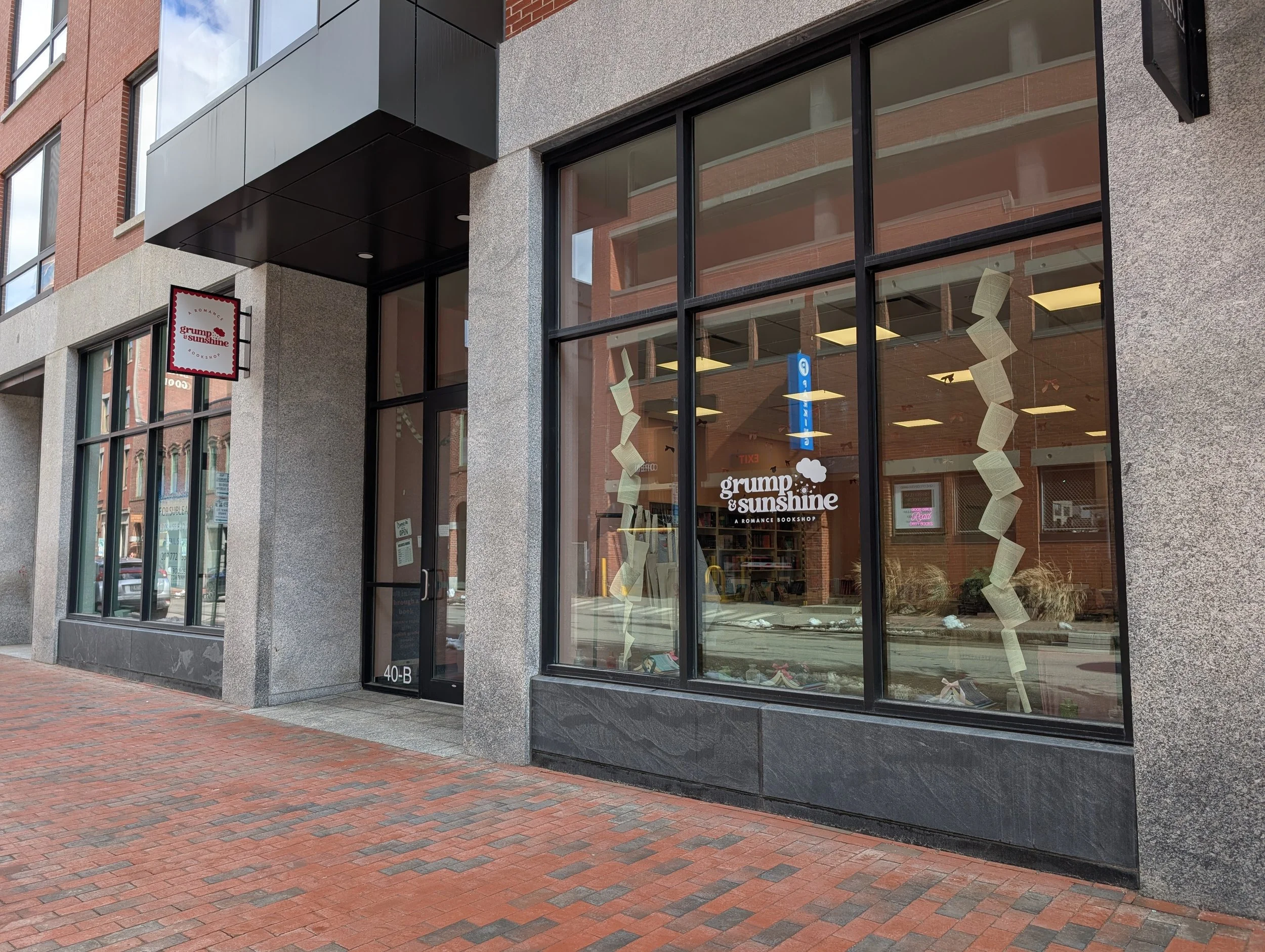 Granite and brick facade with large glass windows and door and a brick sidewalk out front