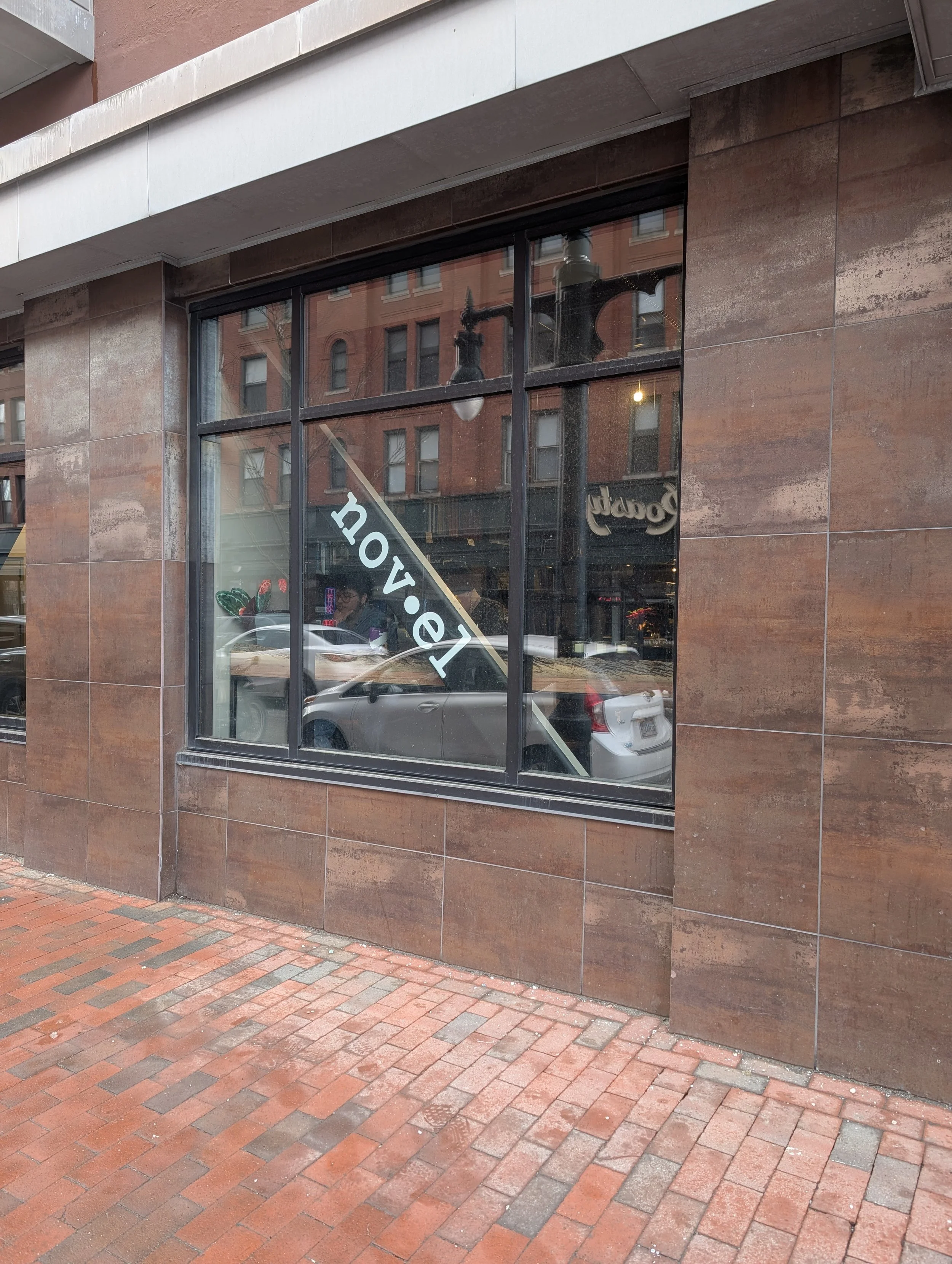 Rusty steel wall with a glass window with the company logo printed on it and a brick sidewalk out front