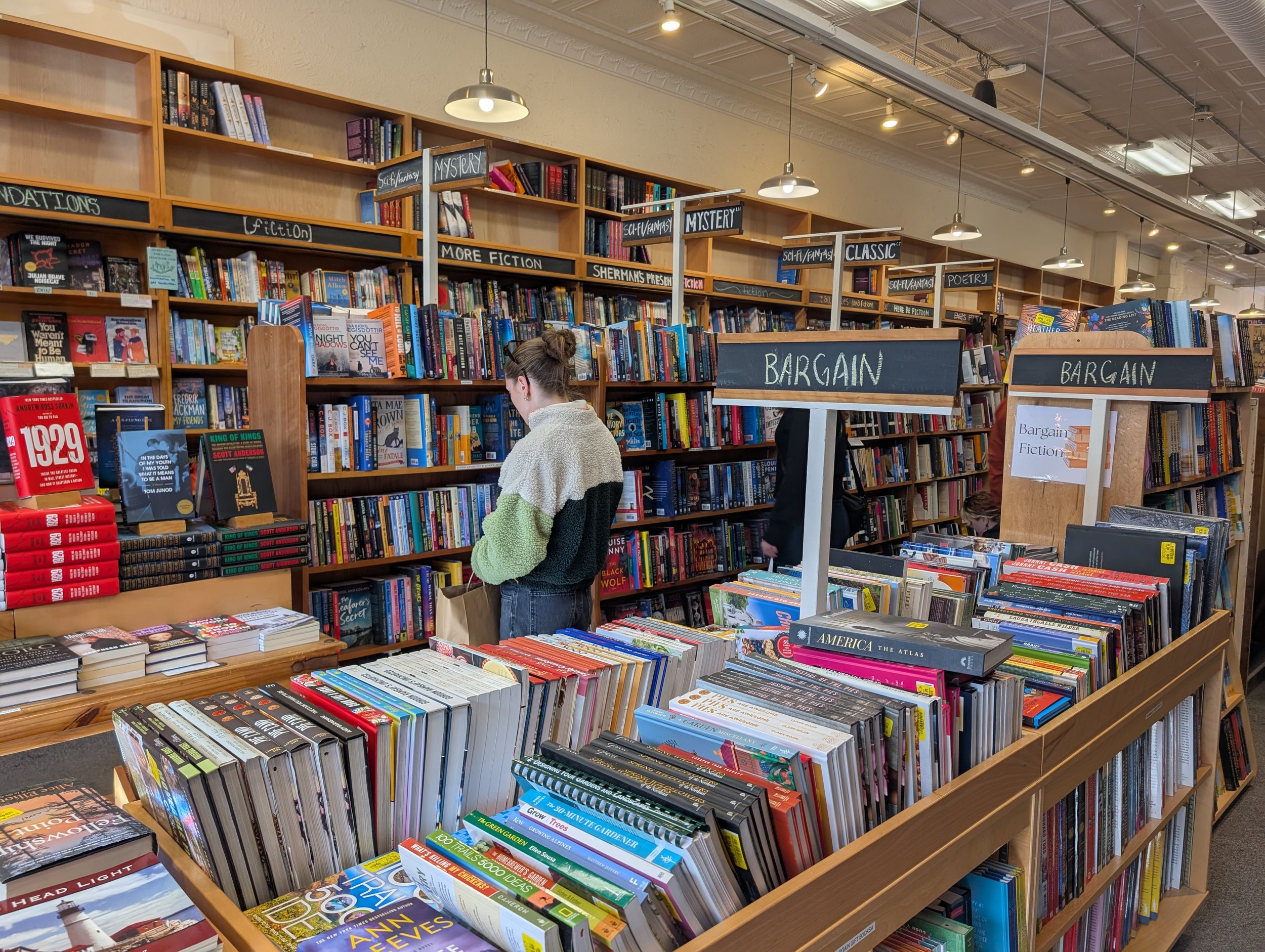 Woman looking at books on a shelf on the wall with a table stacked with books in the foreground