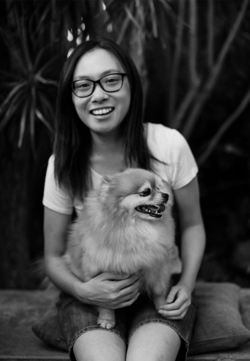 A woman with glasses smiling while holding a fluffy dog outdoors.
