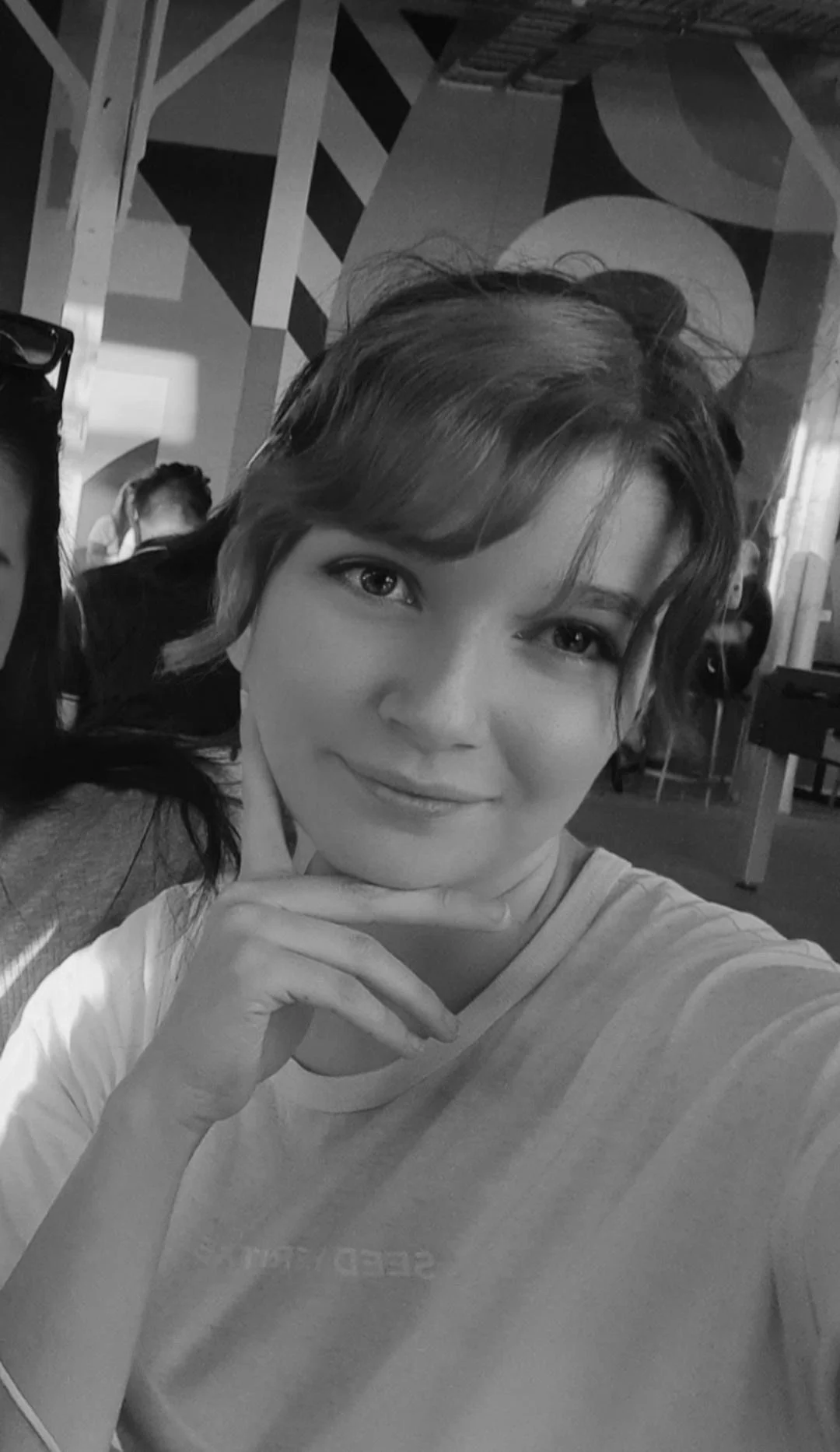 A young woman with short hair, smiling, resting her chin on her hand, in a modern indoor setting.