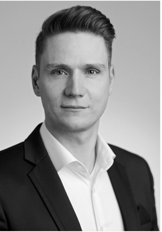 Black and white professional headshot of a young man in a suit and white shirt, looking at the camera with a slight smile.